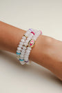 A set of three Leah white bracelets worn on the wrist, featuring milky white beads with colorful accents of pink, blue, and gold, highlighted by a central eye charm.