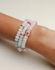 A set of three Leah white bracelets worn on the wrist, featuring milky white beads with colorful accents of pink, blue, and gold, highlighted by a central eye charm.