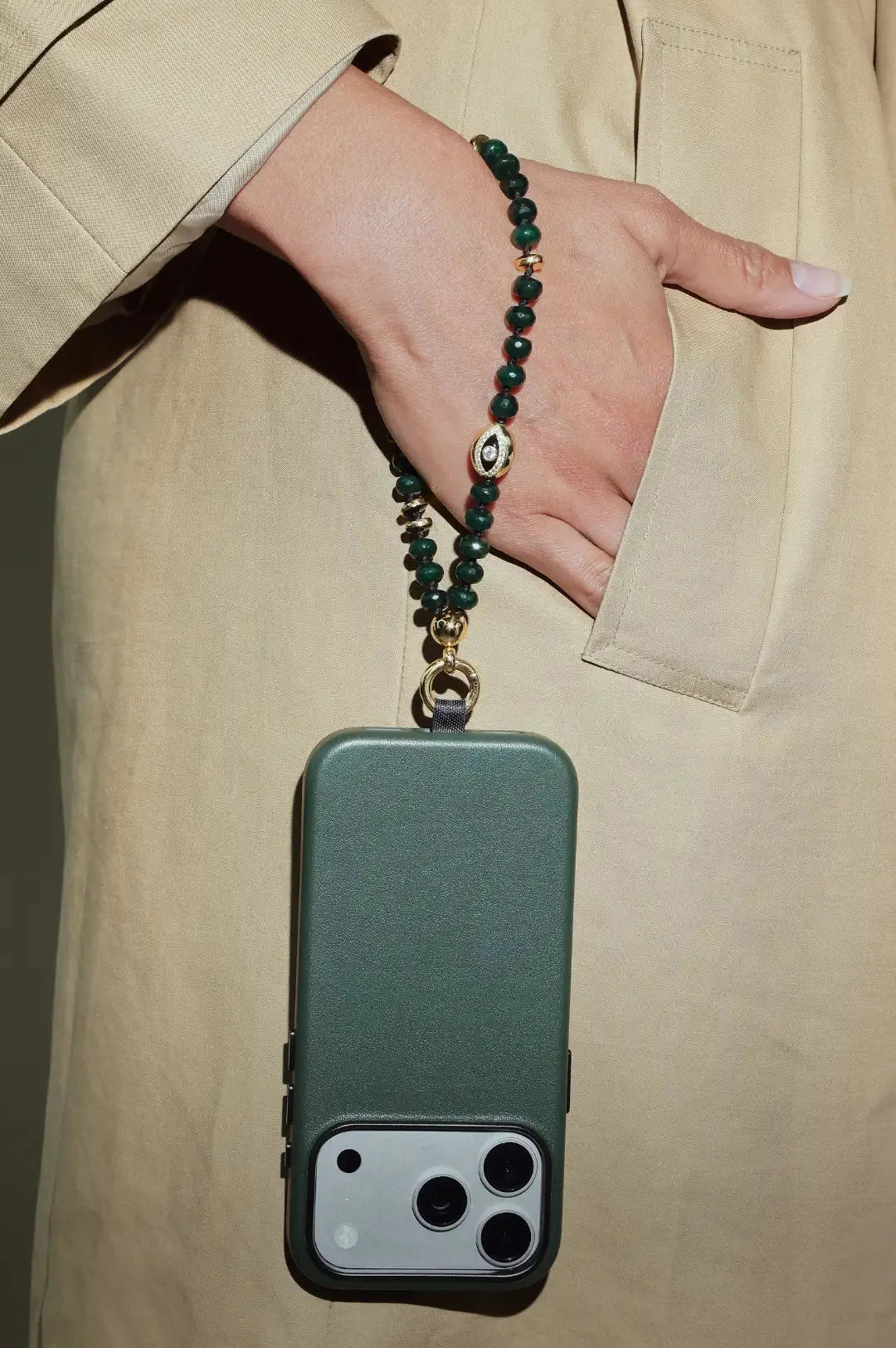 Phone case with a Emerald beaded strap held by a person wearing a beige coat.