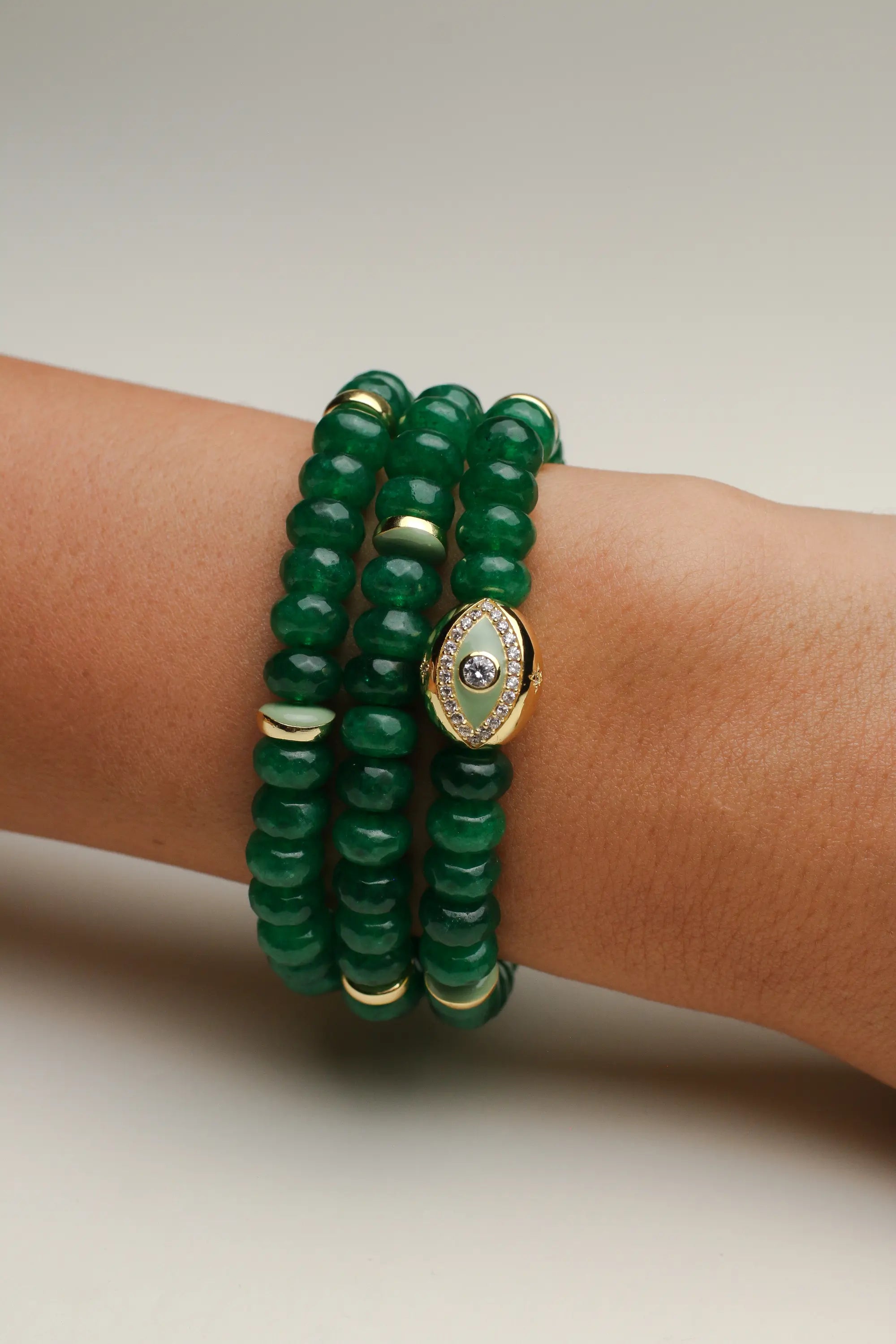 Close-up of the Leah Emerald Bracelet set featuring three stacks of vibrant green quartz beads, accented with gold-plated dividers and an eye charm with CZ diamonds, styled elegantly on a wrist.