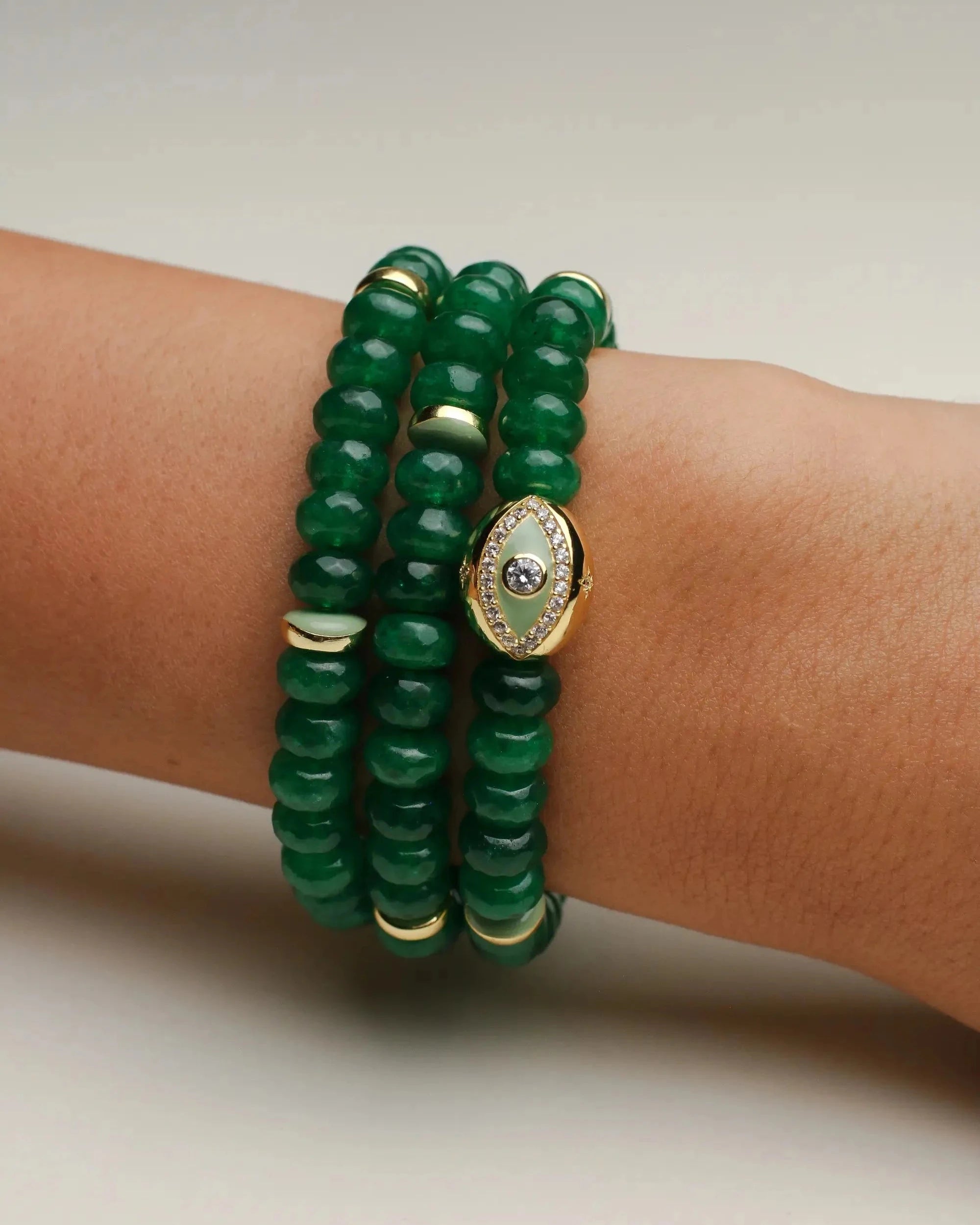 Close-up of the Leah Emerald Bracelet set featuring three stacks of vibrant green quartz beads, accented with gold-plated dividers and an eye charm with CZ diamonds, styled elegantly on a wrist.