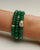 Close-up of the Leah Emerald Bracelet set featuring three stacks of vibrant green quartz beads, accented with gold-plated dividers and an eye charm with CZ diamonds, styled elegantly on a wrist.