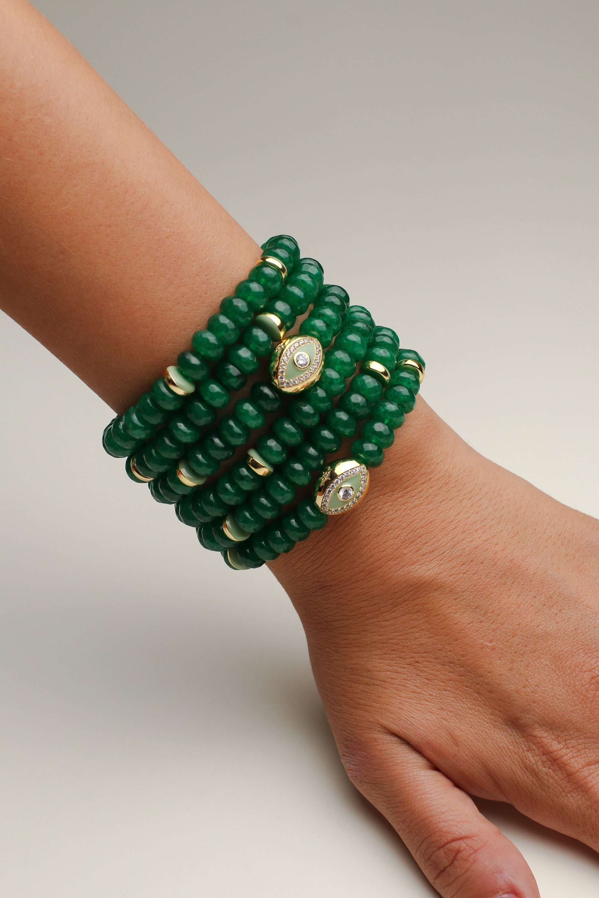 Close-up of the Leah Emerald Bracelet set featuring multiple stacks of deep green quartz beads, enhanced with gold-plated dividers and eye charms adorned with CZ diamonds, elegantly displayed on a wrist. This vibrant and luxurious bracelet set adds a bold statement of style and energy.