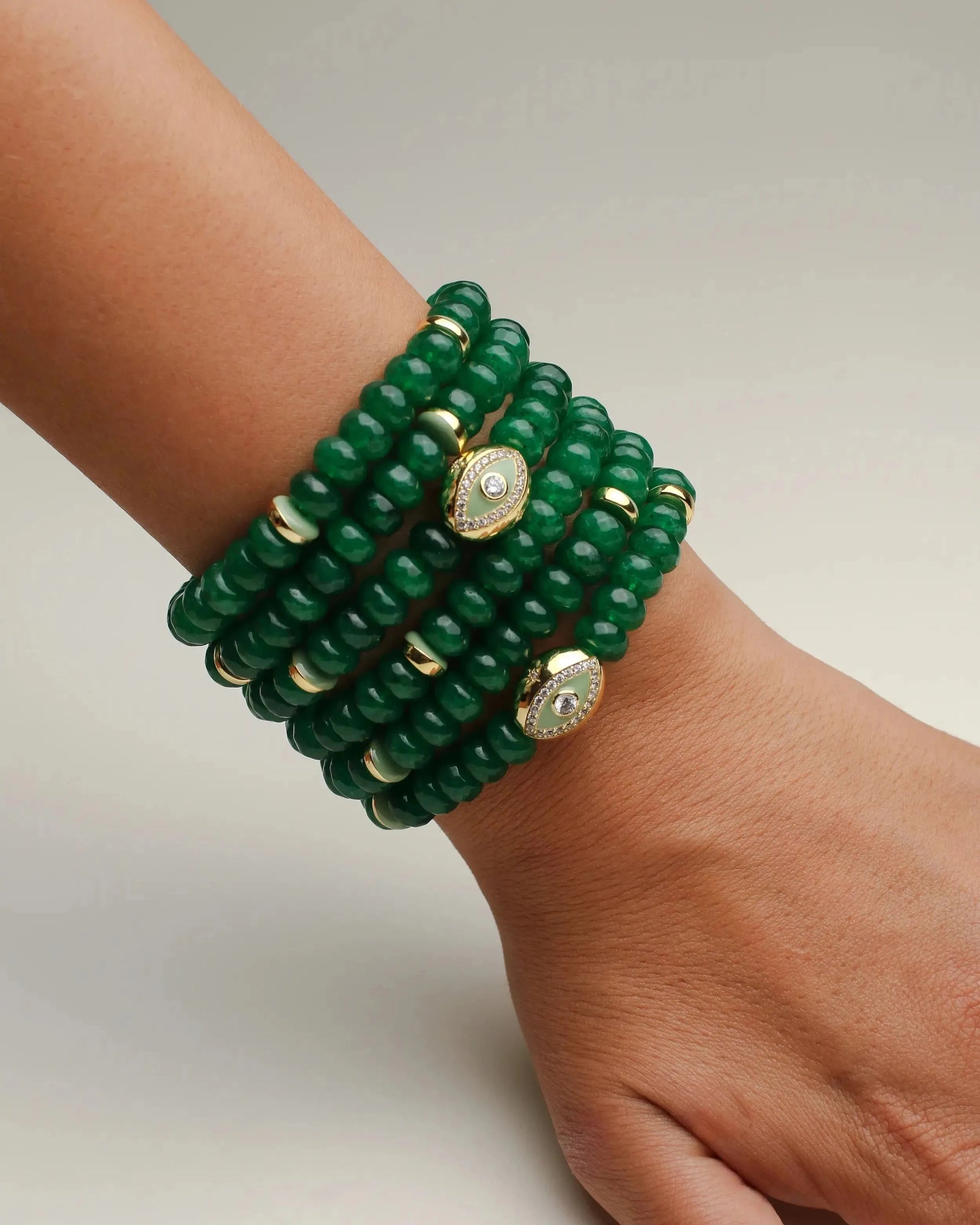 Close-up of the Leah Emerald Bracelet set featuring multiple stacks of deep green quartz beads, enhanced with gold-plated dividers and eye charms adorned with CZ diamonds, elegantly displayed on a wrist. This vibrant and luxurious bracelet set adds a bold statement of style and energy.