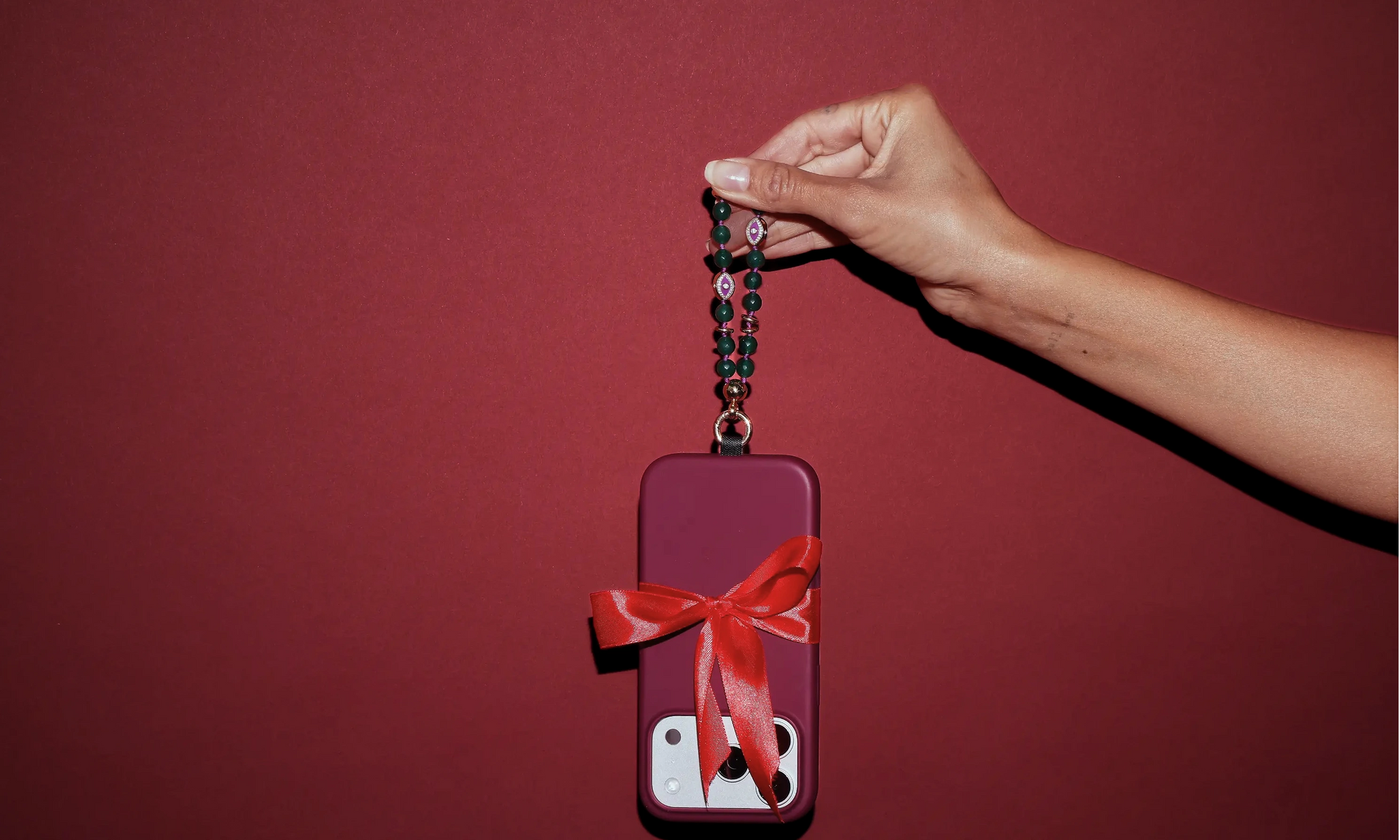 Phone case with a red bow held by a phone charm with hand against a red background