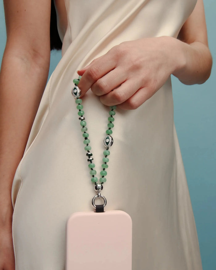 Full view of the Jade Leah Phone Charm paired with a blush phone case, held by a model in a cream outfit.