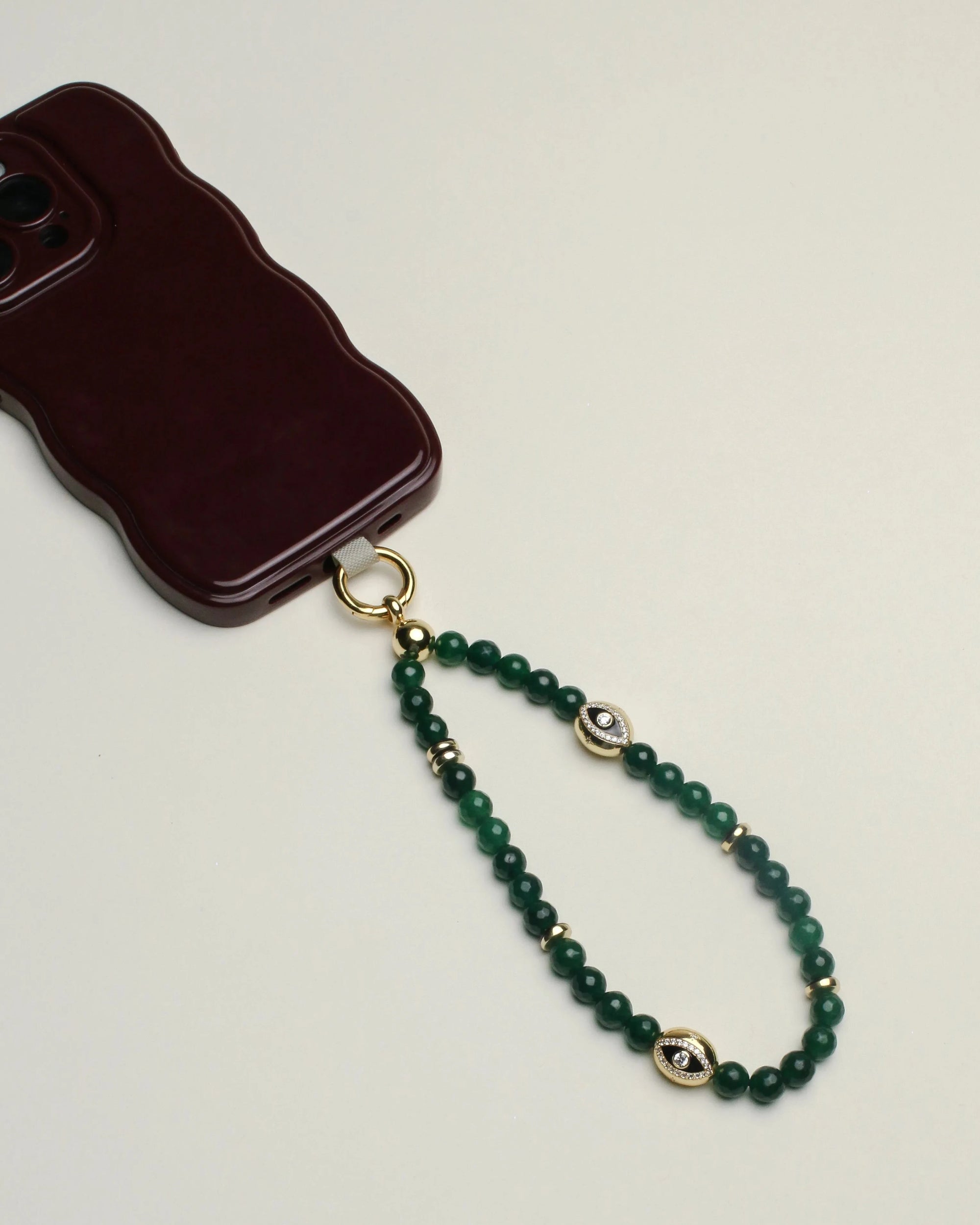 Close-up of the Leah wristlet in emerald quartz, highlighting the deep green beads, gold accents, and a central charm, paired with a phone case for a stylish touch.