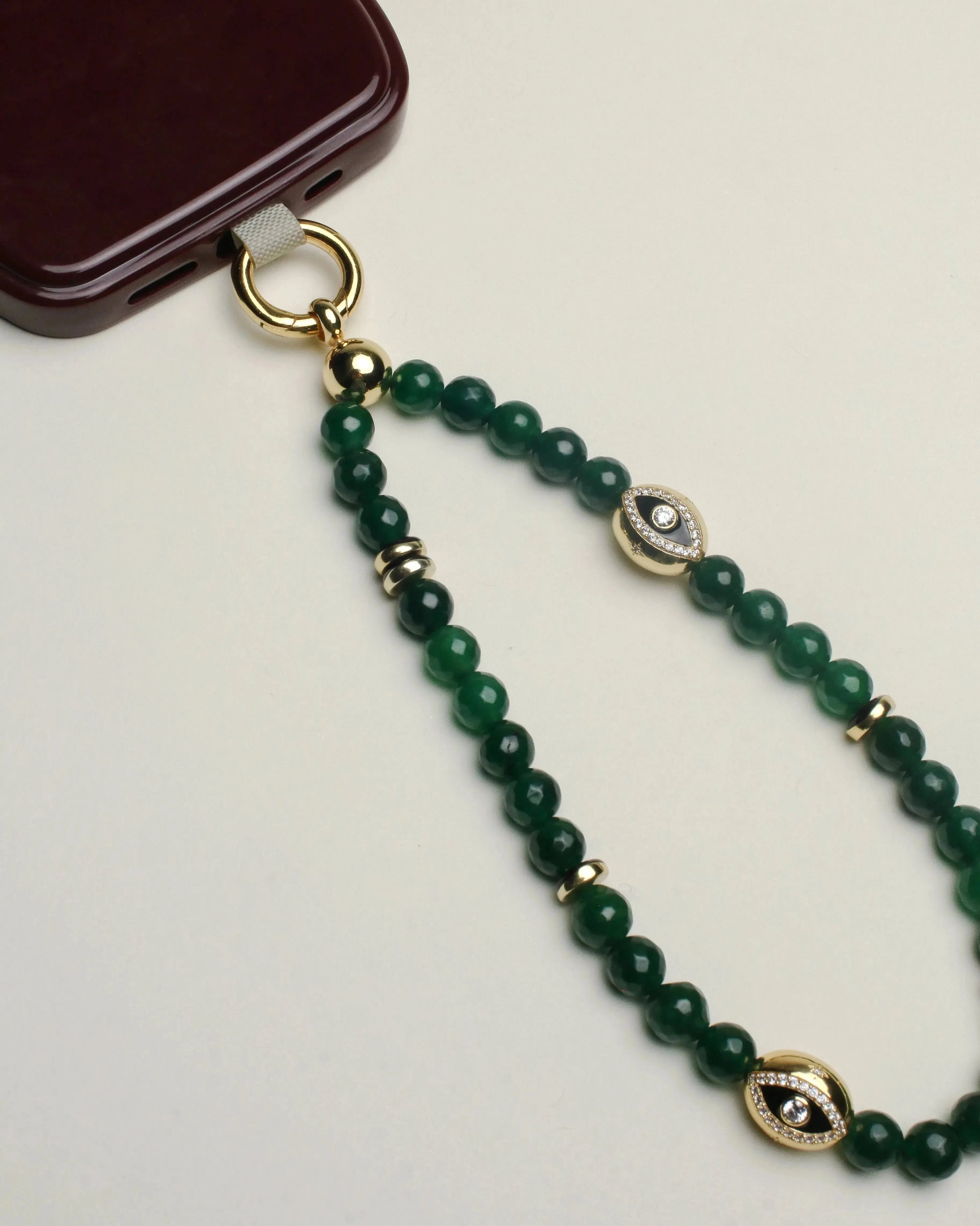 Leah emerald wristlet displayed connected to a burgundy phone case, showcasing the vibrant green beads and gold detailing, complete with a central decorative charm.