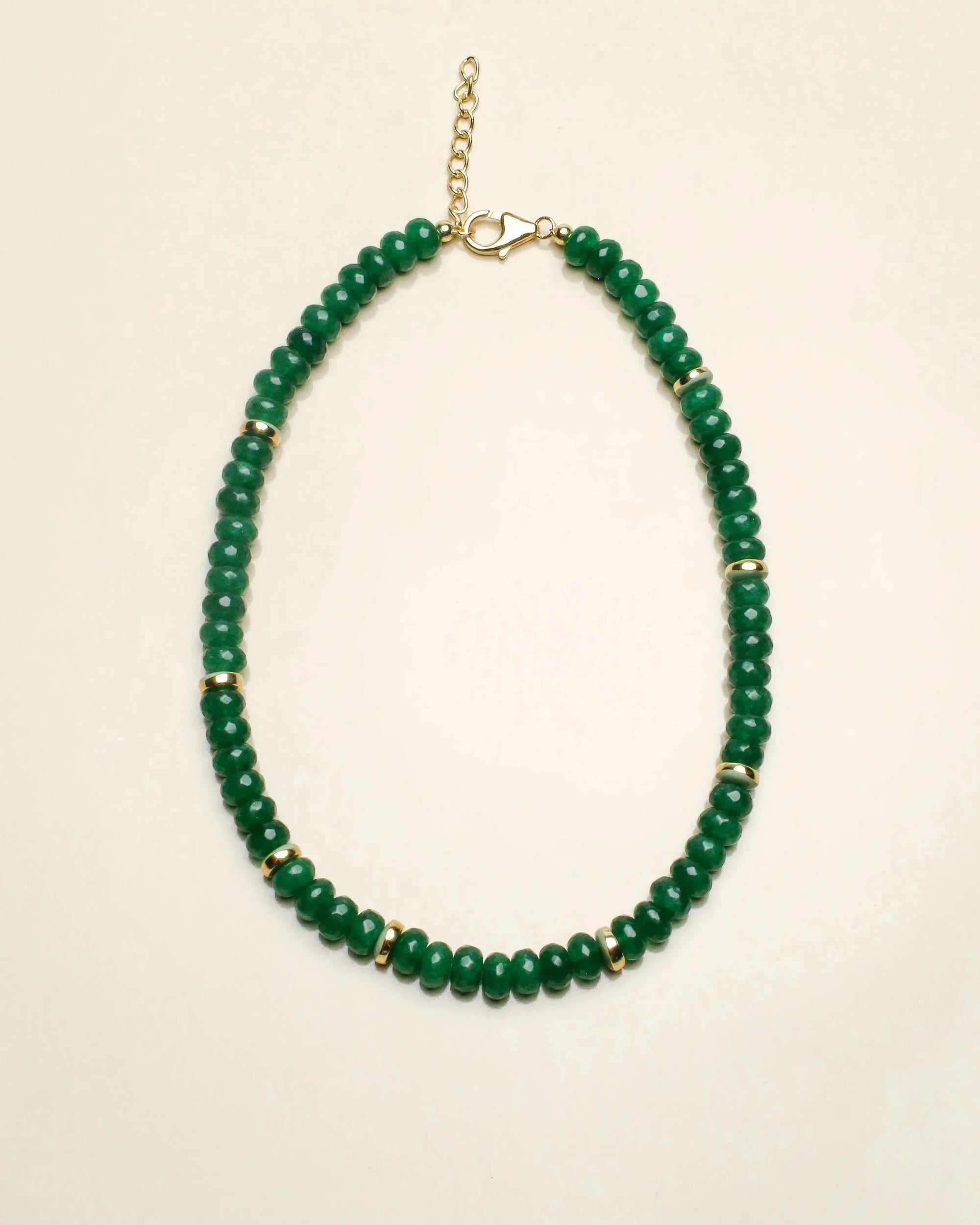 lilou emerald beaded necklace with gold accents, styled with a light cream cardigan. The jewelry showcases vibrant green quartz beads, emphasizing elegance and balance.