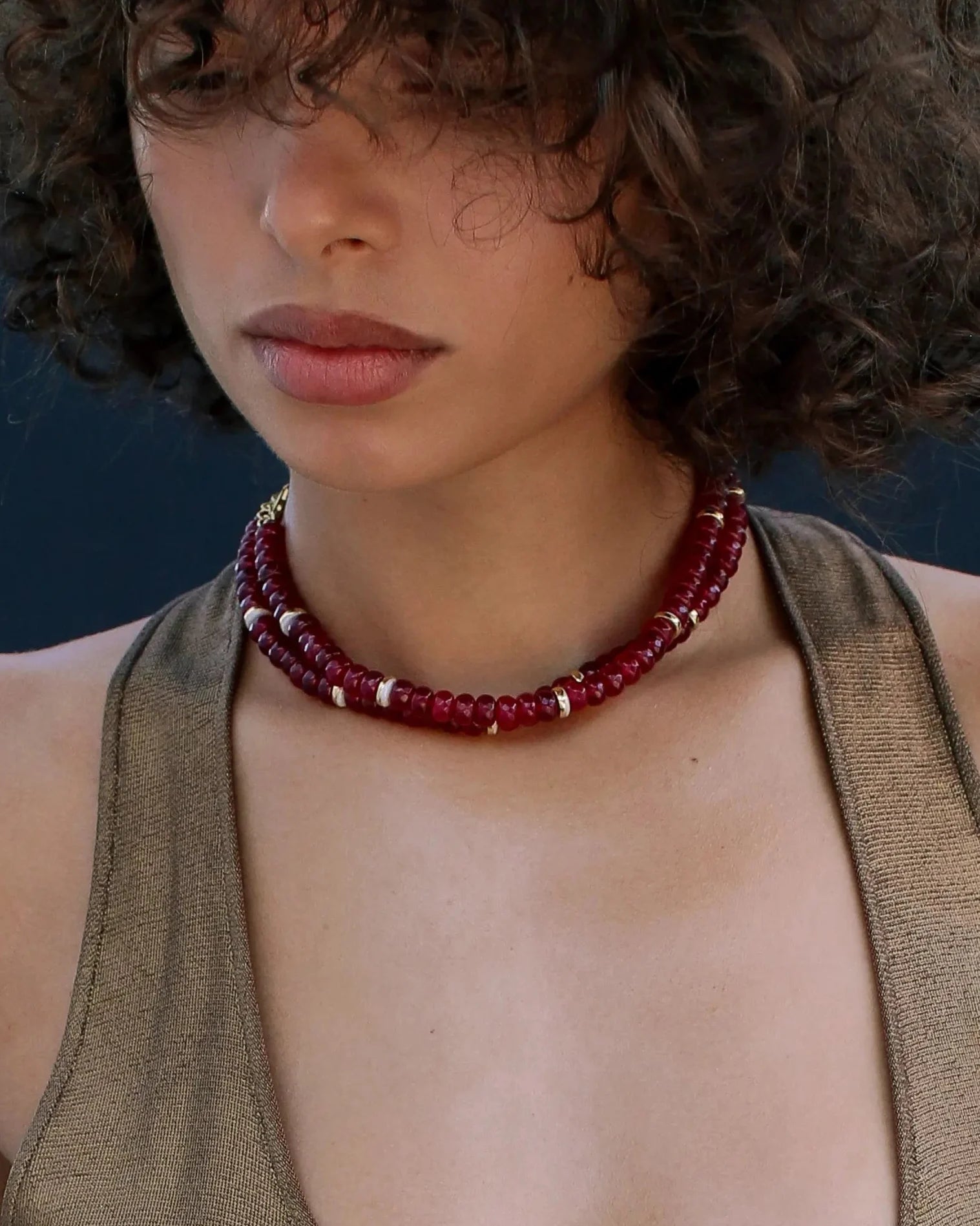 A close-up of a woman wearing a layered cherry beaded necklace with gold accents, elegantly paired with a neutral-toned sleeveless top, emphasizing a chic and sophisticated style.