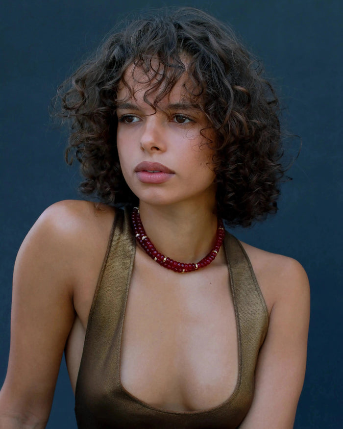 Model wearing the Lilou necklace in cherry quartz, showcasing the vibrant red beads and gold accents against the skin for a bold, statement look.