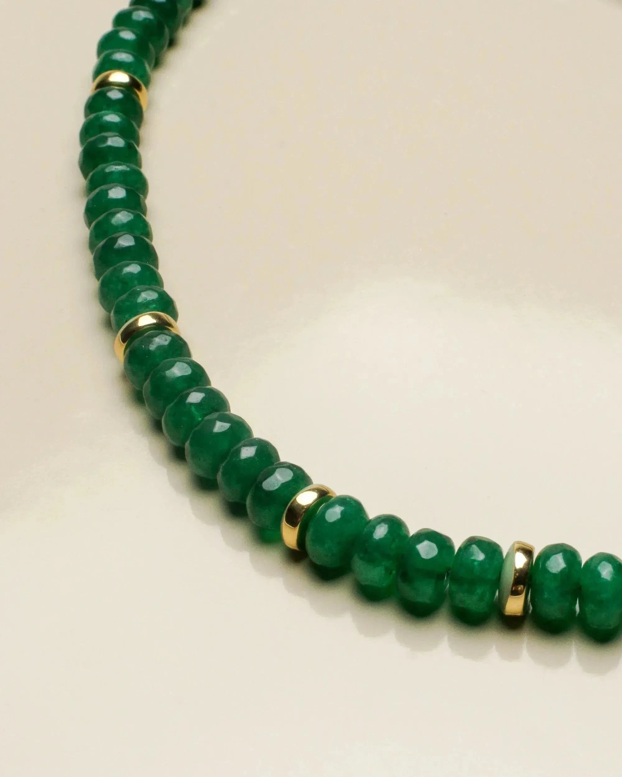 Woman wearing the lilou emerald beaded necklace and matching leah emerald bracelet stack with gold accents, styled with a light cream cardigan. The jewelry showcases vibrant green quartz beads, emphasizing elegance and balance.