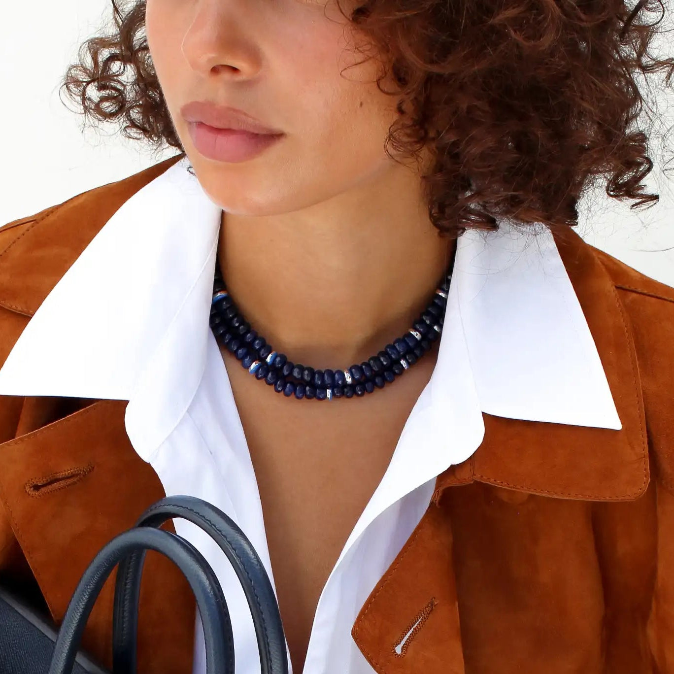 Person holding a black handbag with visible brand logo, wearing a brown jacket and blue jeans.