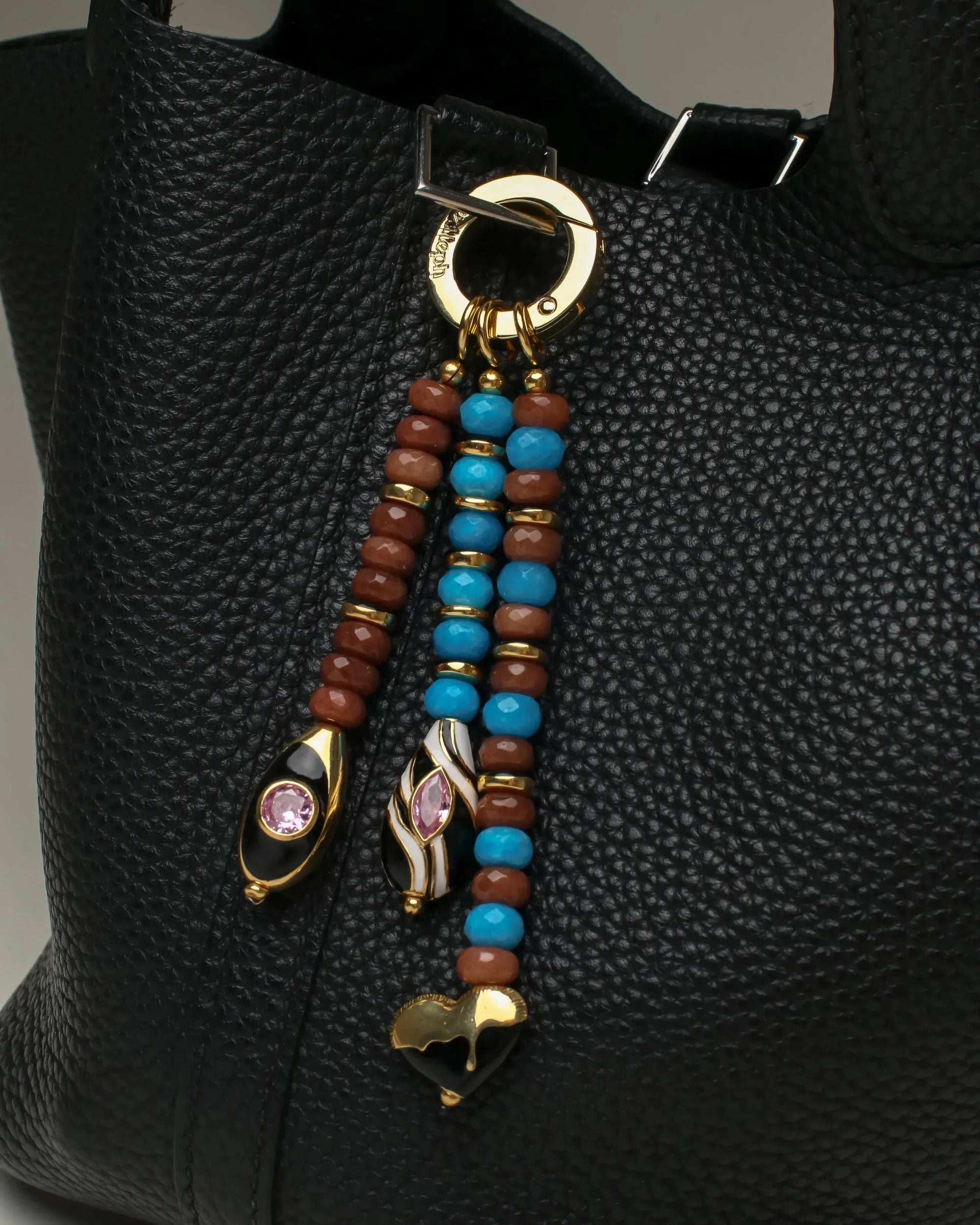 The Liora Bag Charm in Azure & Espresso attached to a black leather bag, adding an elegant and colorful accent.