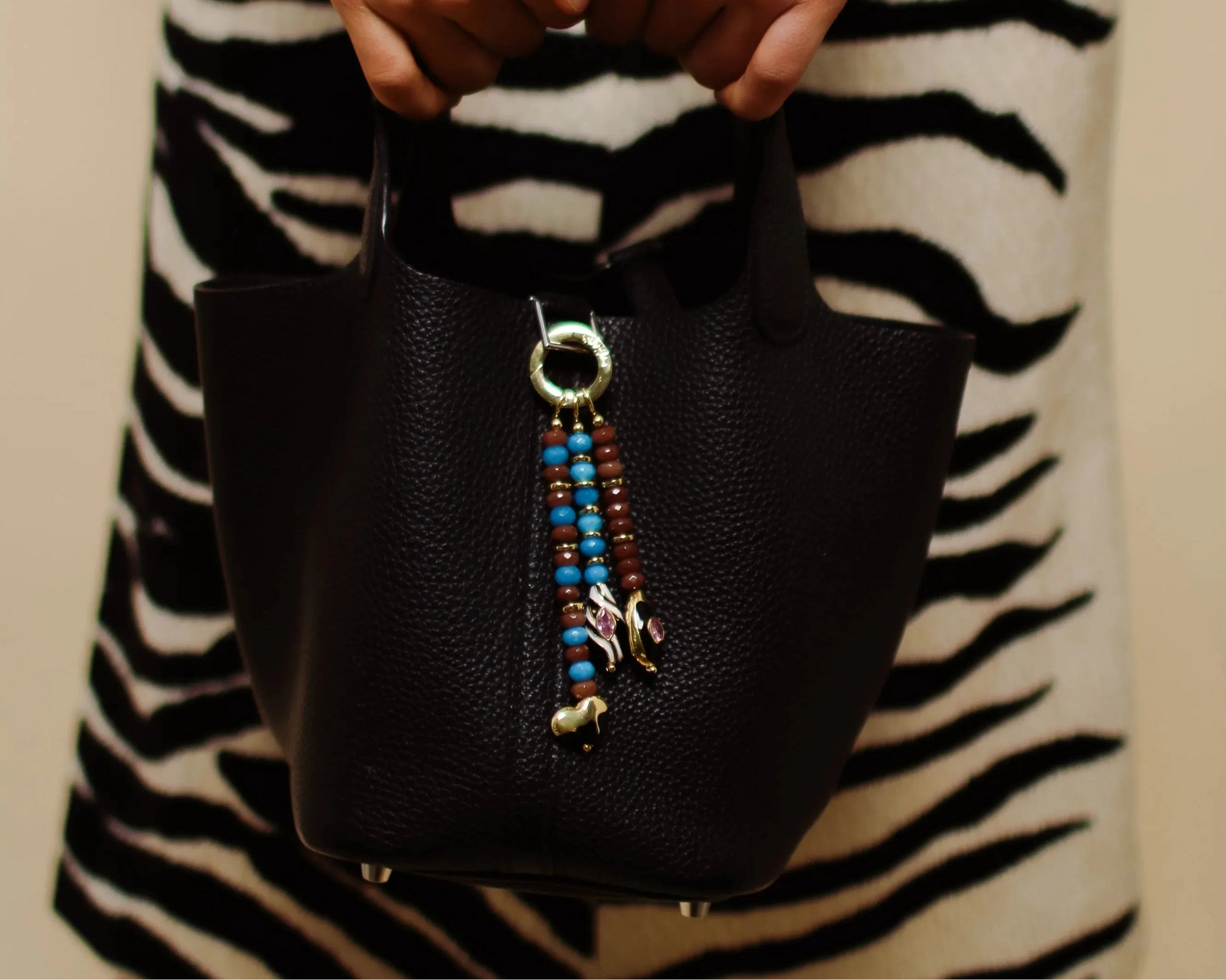 Black handbag with colorful bag charm held by a person wearing a zebra-striped sweater.