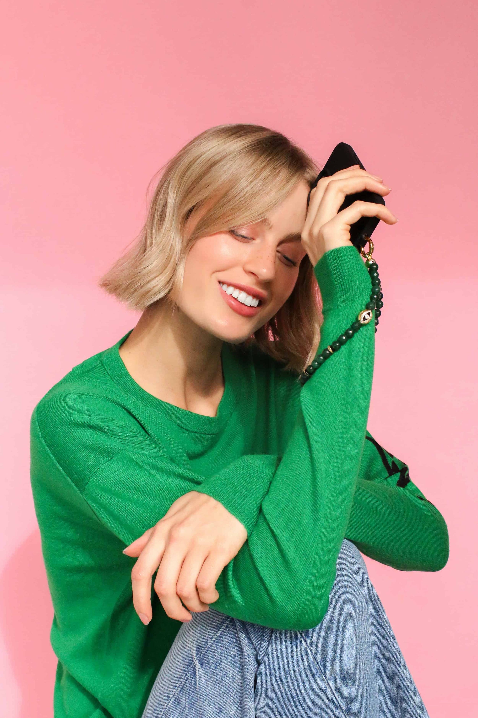 a woman in green sweater with a an emerald wristlet phone strap around her wrist