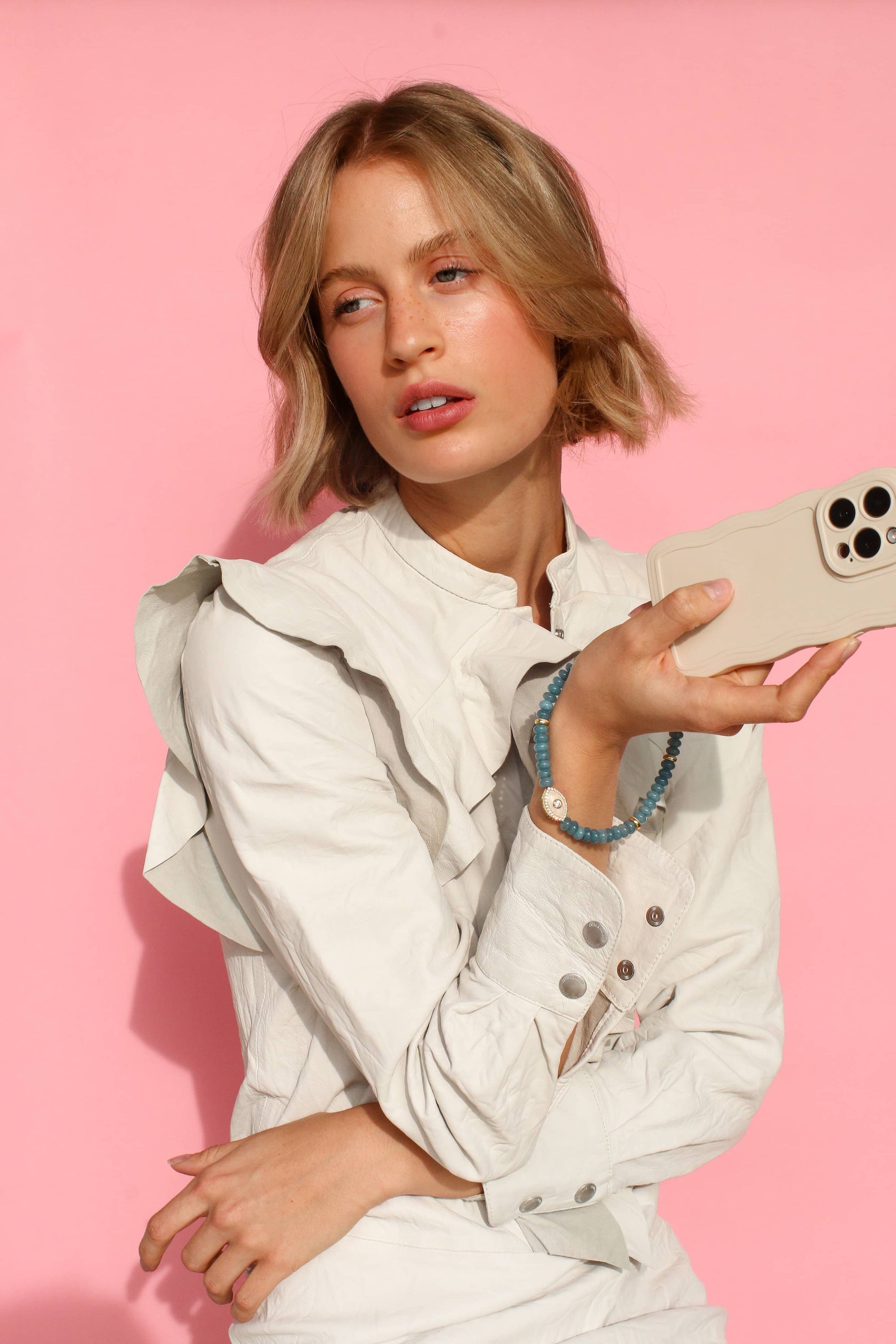 a woman in a white jacket holding her phone, with its apatite quartz phone strap around her wrist