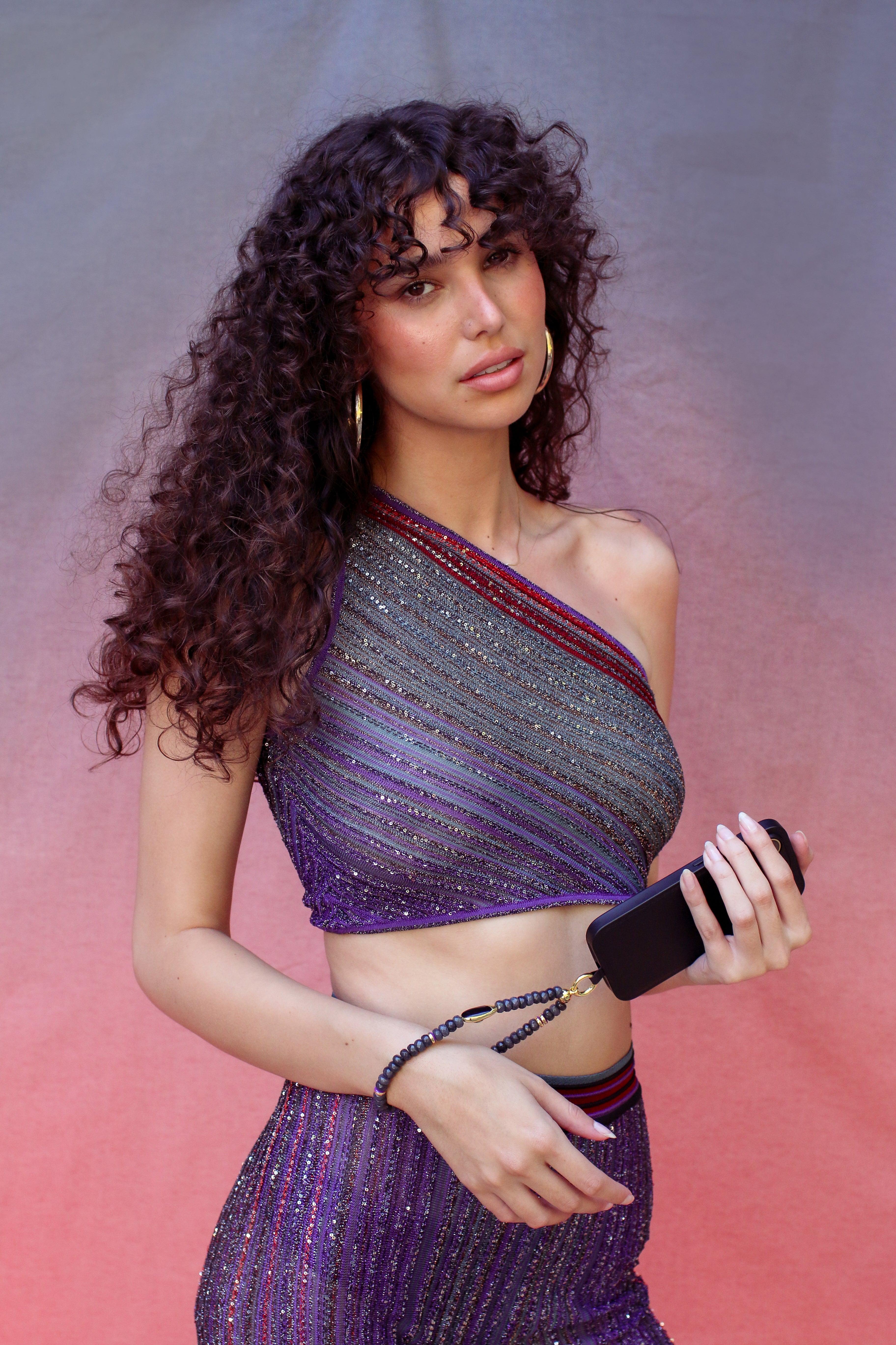 A young woman holding a black phone with its beaded strap around her wrist