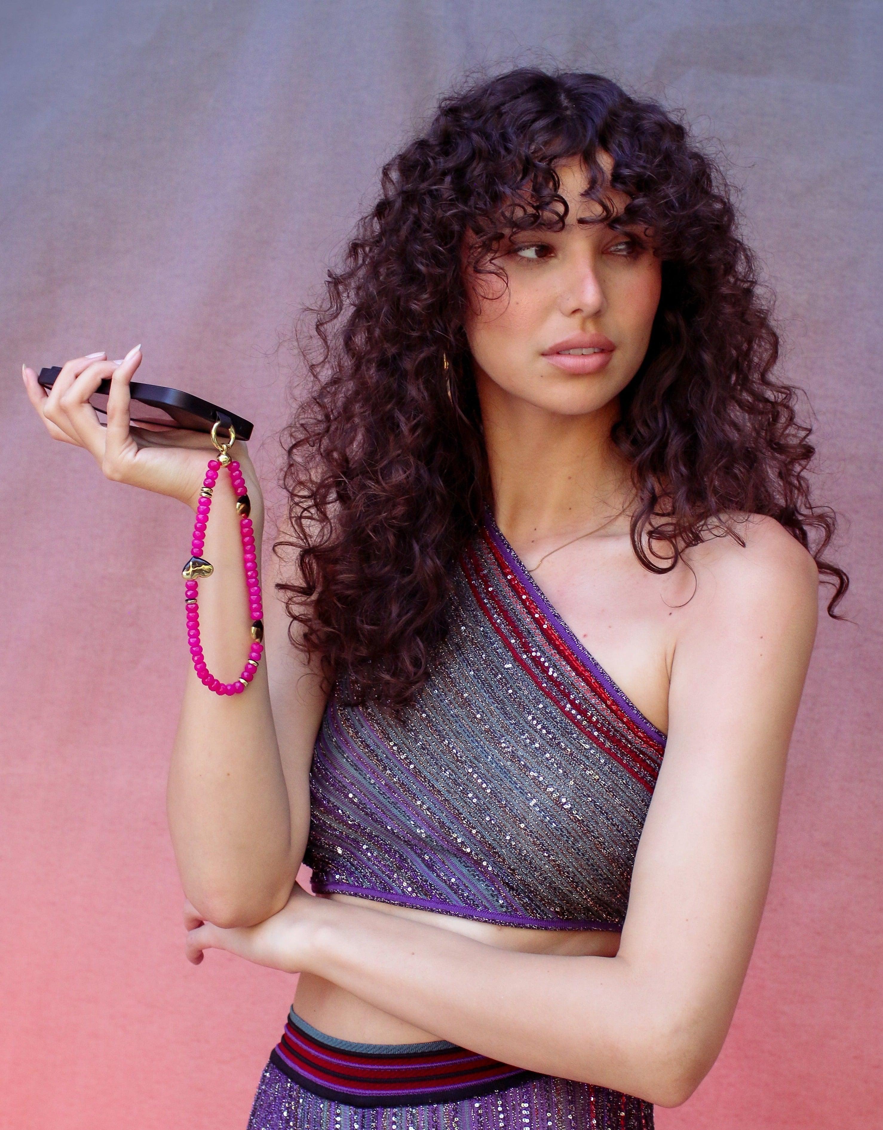 Woman in violet clothes holding a phone with a pink beaded strap