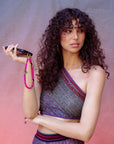 Woman in violet clothes holding a phone with a pink beaded strap