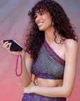 A smiling woman holding a black mobile phone with a hot pink beaded strap