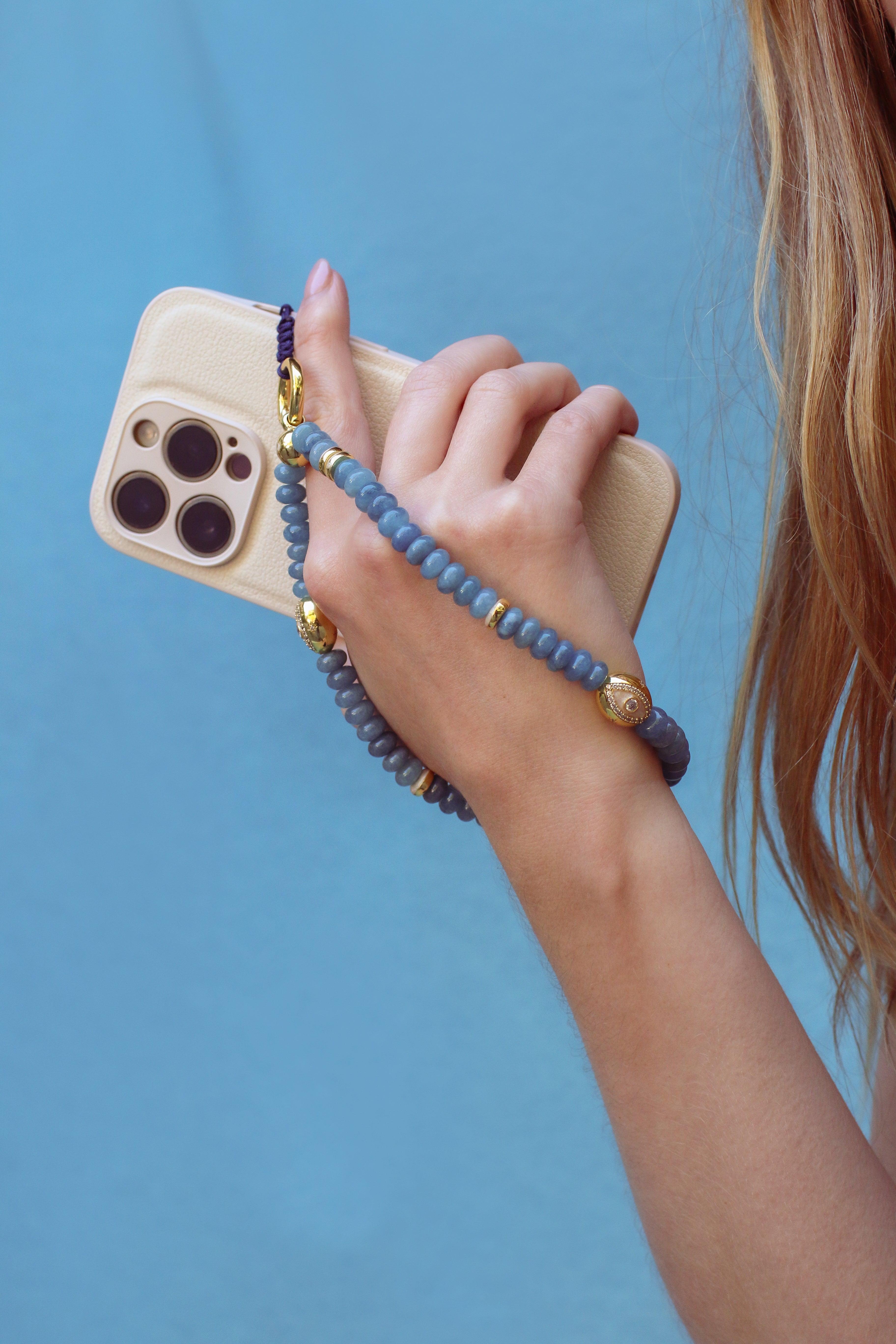 Close-up of a hand holding a white phone, with its blue beaded strap worn around the wrist