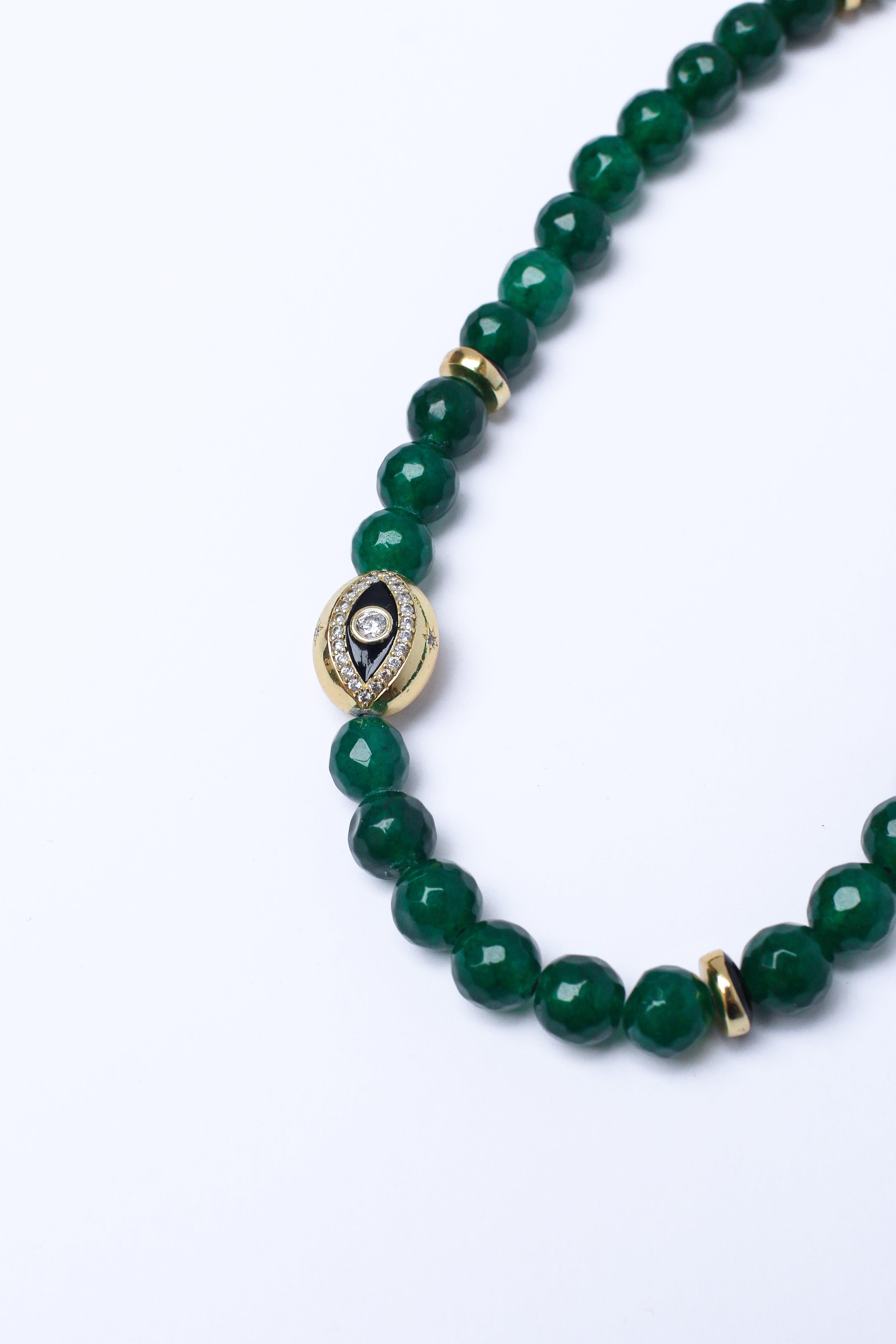 Close-up of a green beaded phone strap with an evil eye charm on a white surface