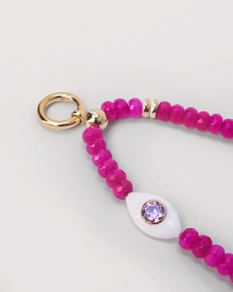 The Mano phone wristlet in hot pink quartz displayed flat, showcasing the bright pink beads, gold accents, and a decorative white charm with a central pink gemstone."

Image 3: "Person holding a phone with the Mano wristlet in hot pink quartz attached, featuring striking pink beads and a decorative white charm, adding a pop of color to their outfit.