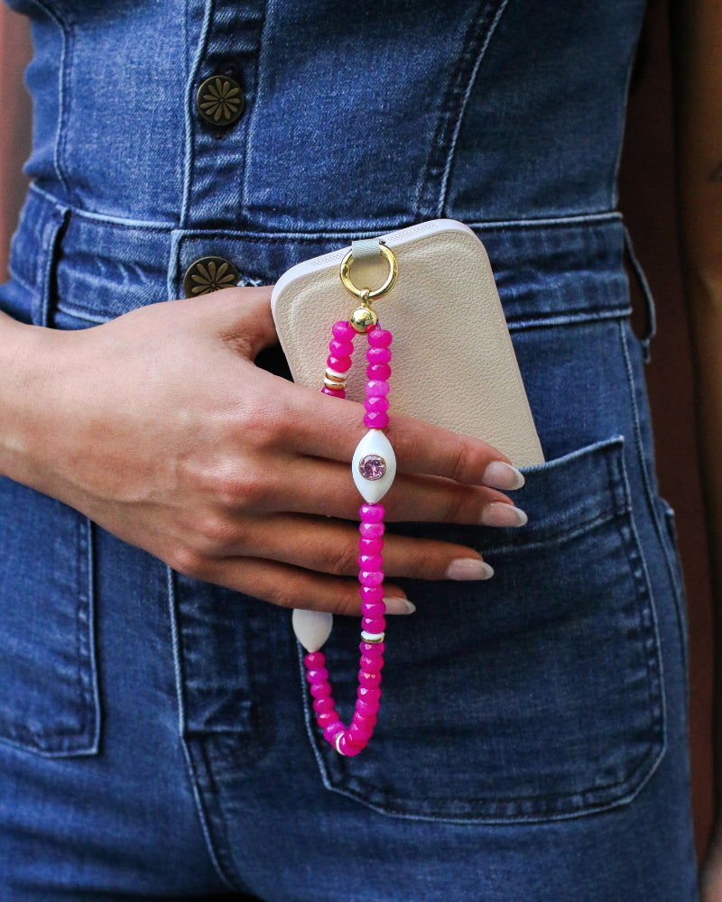 Mano phone wristlet in hot pink quartz being used as a phone strap, highlighting the vivid pink beads, gold accents, and a white charm with a pink gemstone for a playful, stylish touch.