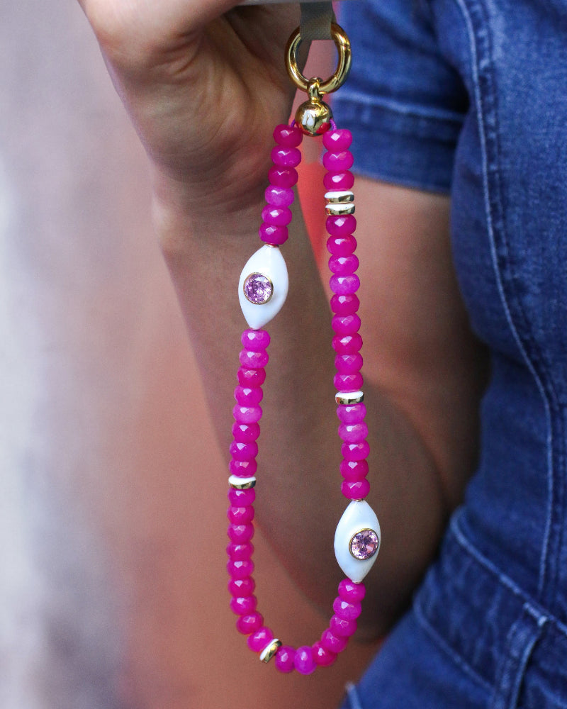 Person holding a phone with the Mano wristlet in hot pink quartz attached, featuring striking pink beads and a decorative white charm, adding a pop of color to their outfit.