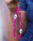 Person holding a phone with the Mano wristlet in hot pink quartz attached, featuring striking pink beads and a decorative white charm, adding a pop of color to their outfit.