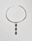 Gold collar necklace with three black enamel evil eye charms displayed against a white background.