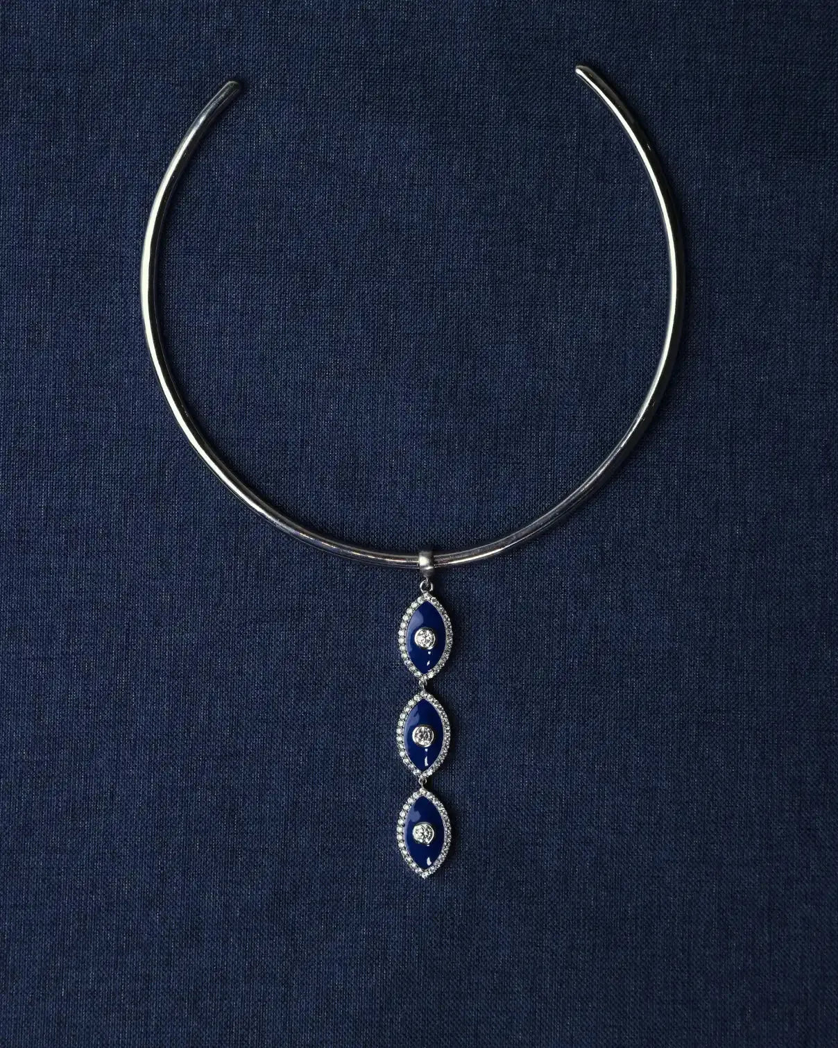 Silver choker necklace with blue evil eye pendant on a dark blue fabric background