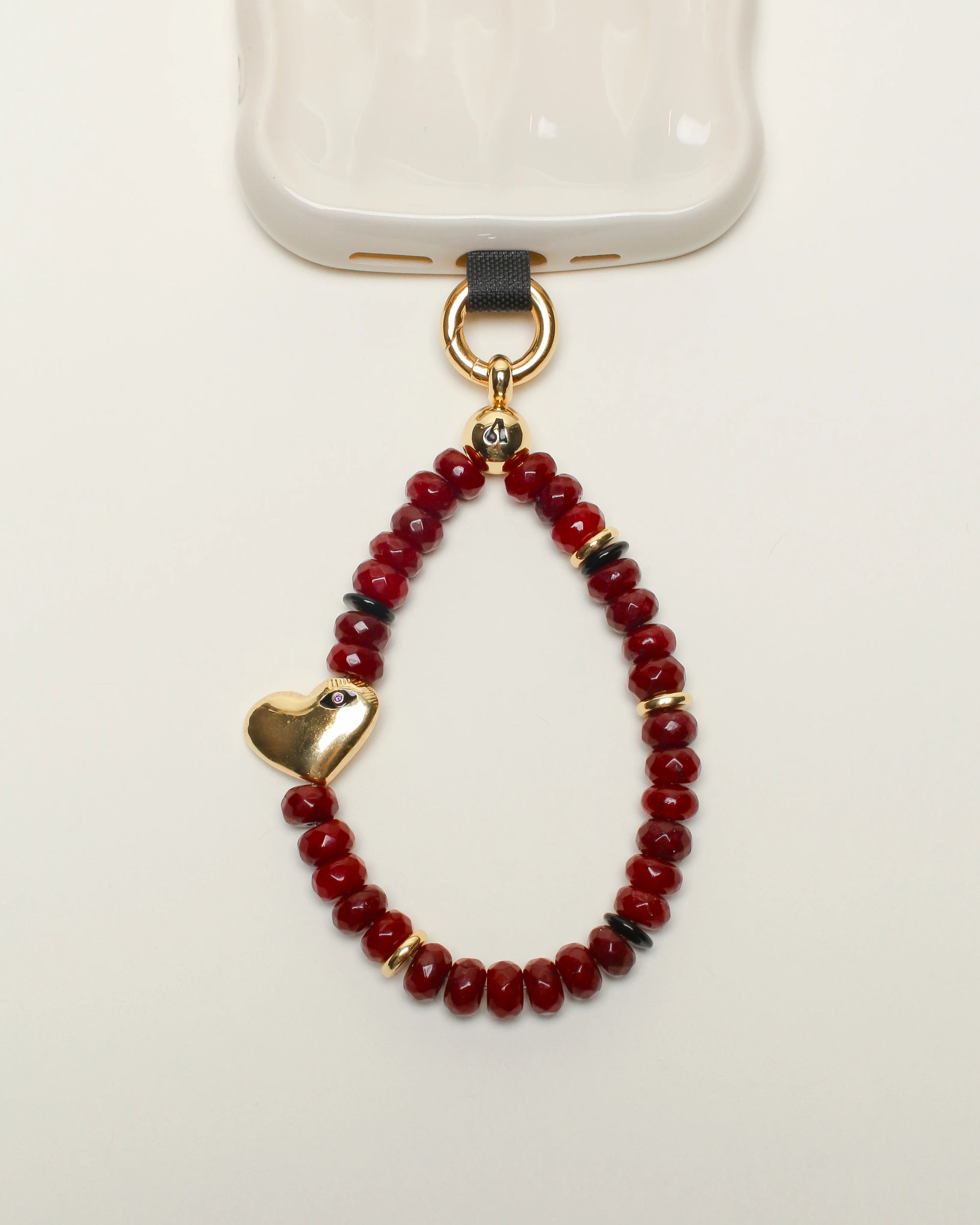 Close-up of Mini Noelle Wristlet in Cherry Quartz – A petite wristlet made of vibrant cherry quartz beads, featuring a gold heart charm, attached to a phone for a stylish and functional accessory.