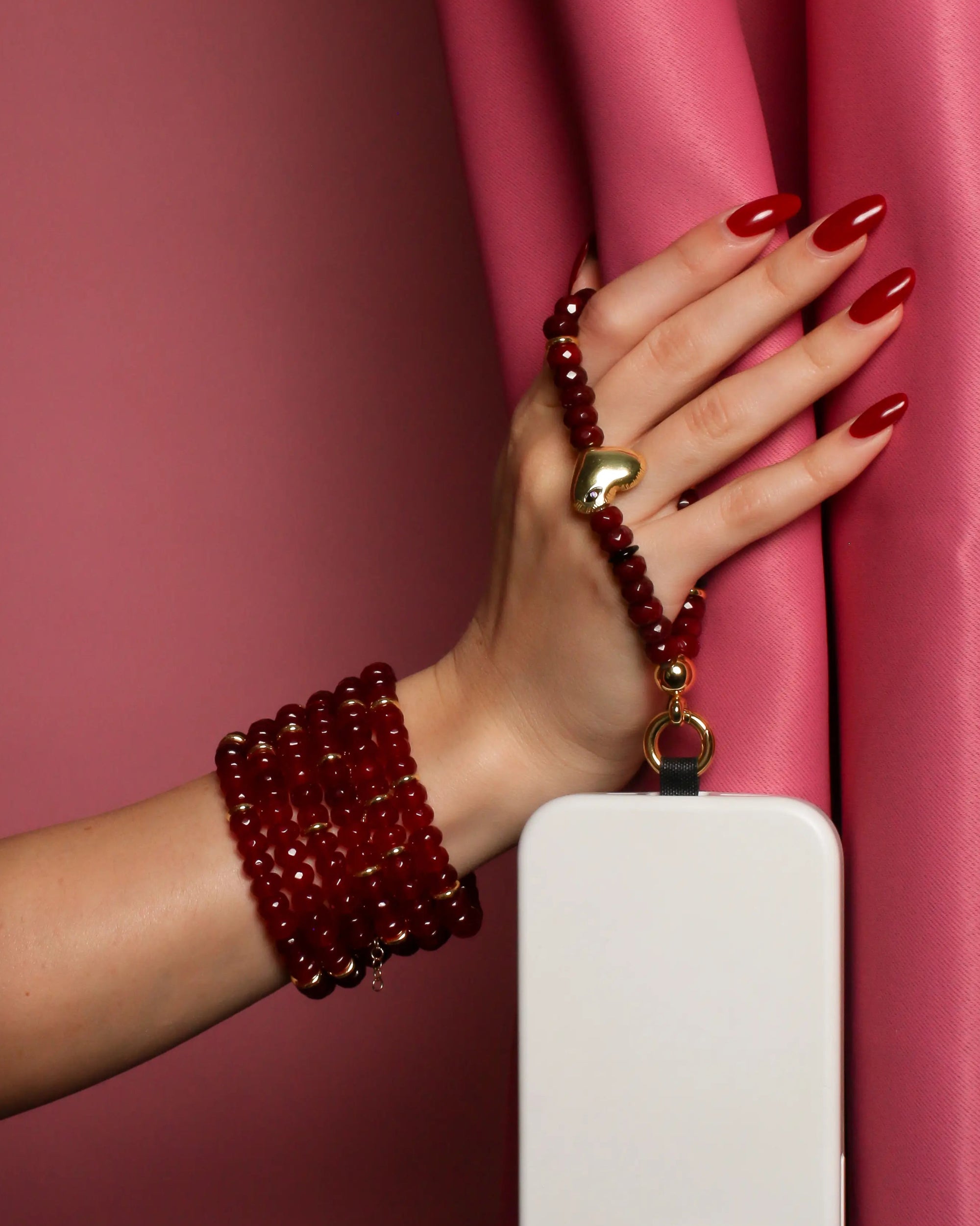 Hand modeling Mini Noelle Wristlet with stacked bracelets – A hand adorned with multiple cherry quartz bracelets, elegantly posed against a pink curtain, showcasing the wristlet's bold and fashionable look.