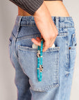 Person wearing the Minou wristlet in turquoise quartz, shown clipped to jeans, highlighting its stylish blend of vibrant beads and protective zebra-patterned evil eye charm.