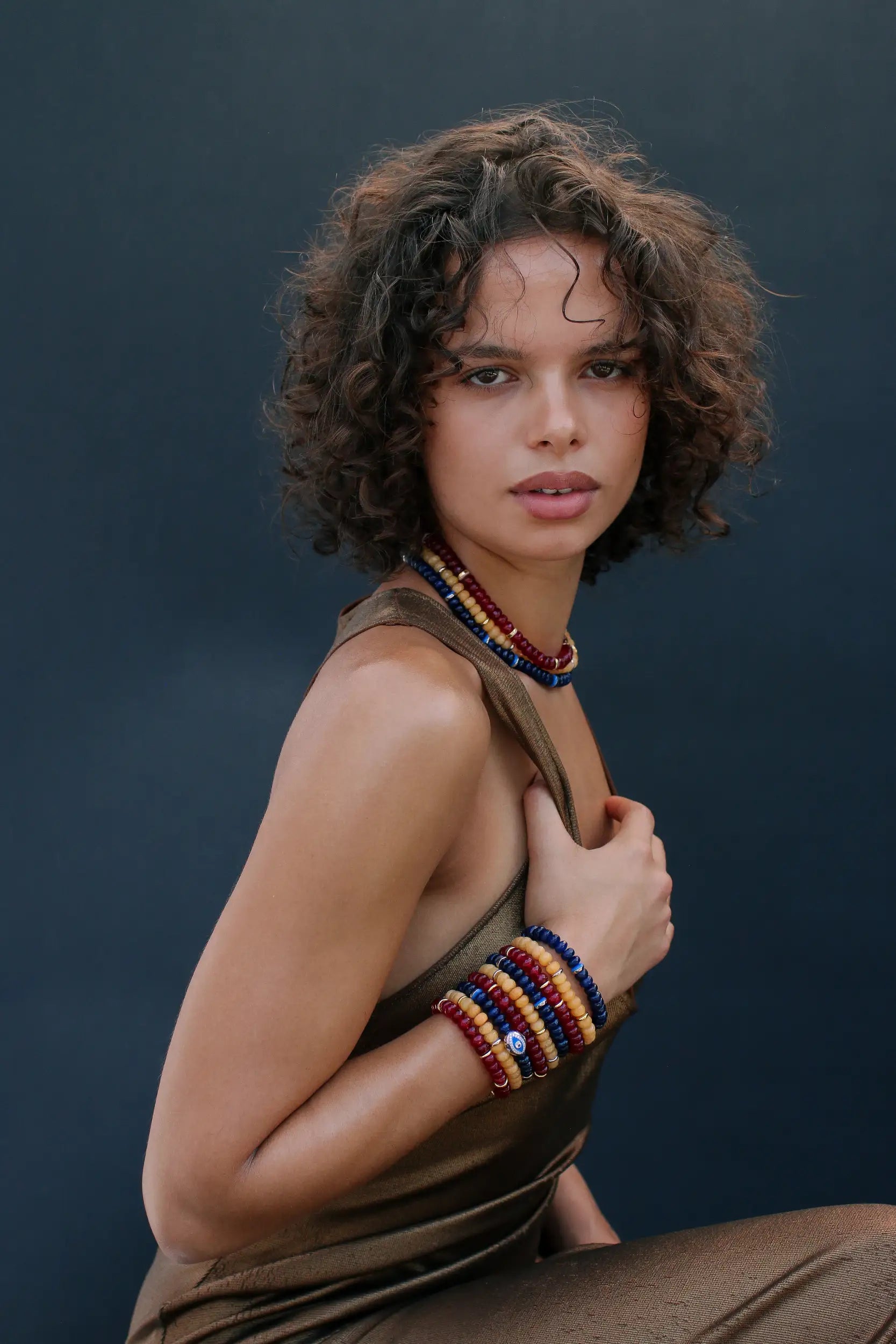 Woman wearing a sleeveless top and colorful beaded accessories against a dark background