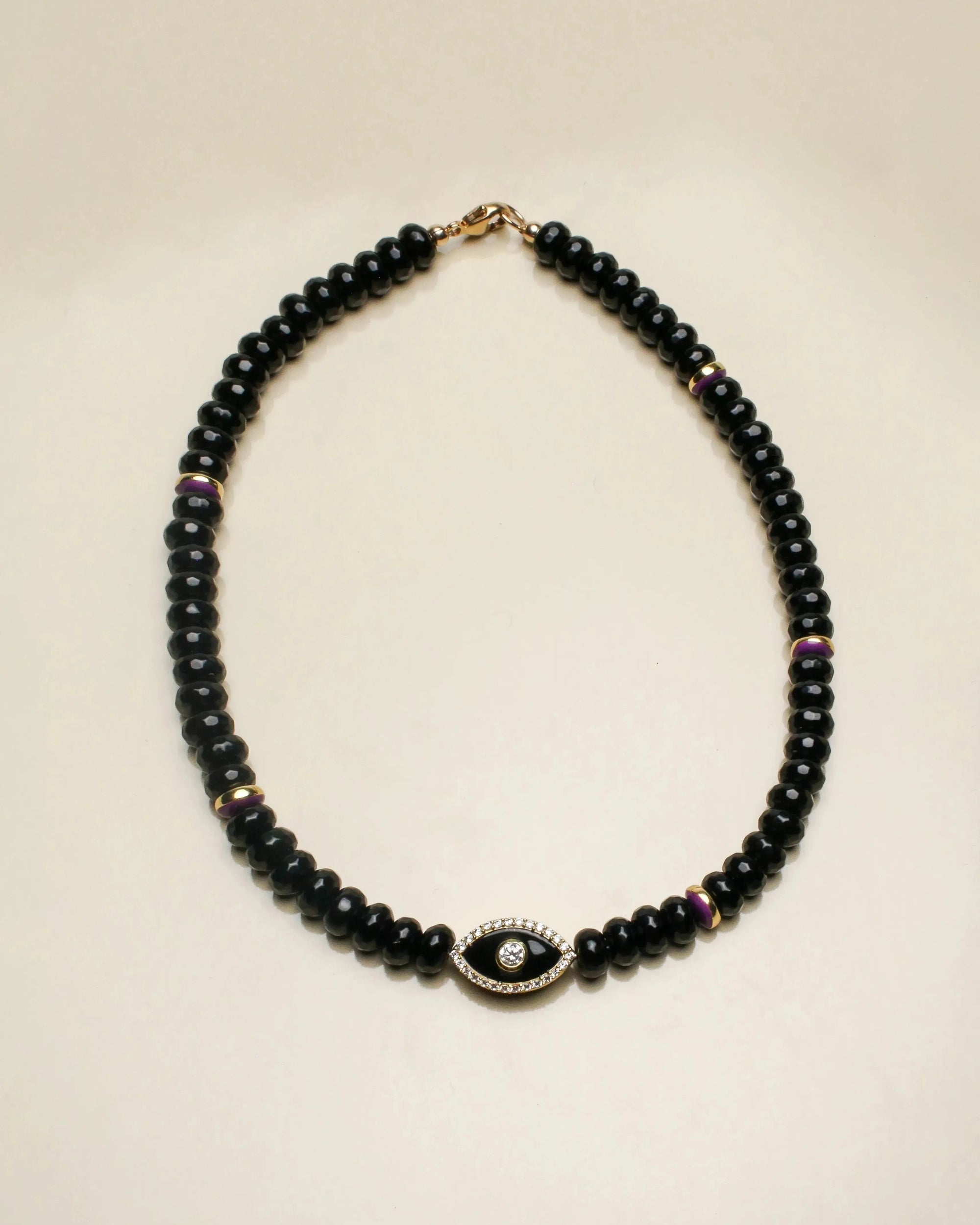 Stella necklace featuring deep black onyx beads and a central evil eye-shaped charm in gold with detailed accents, offering a bold and elegant statement.