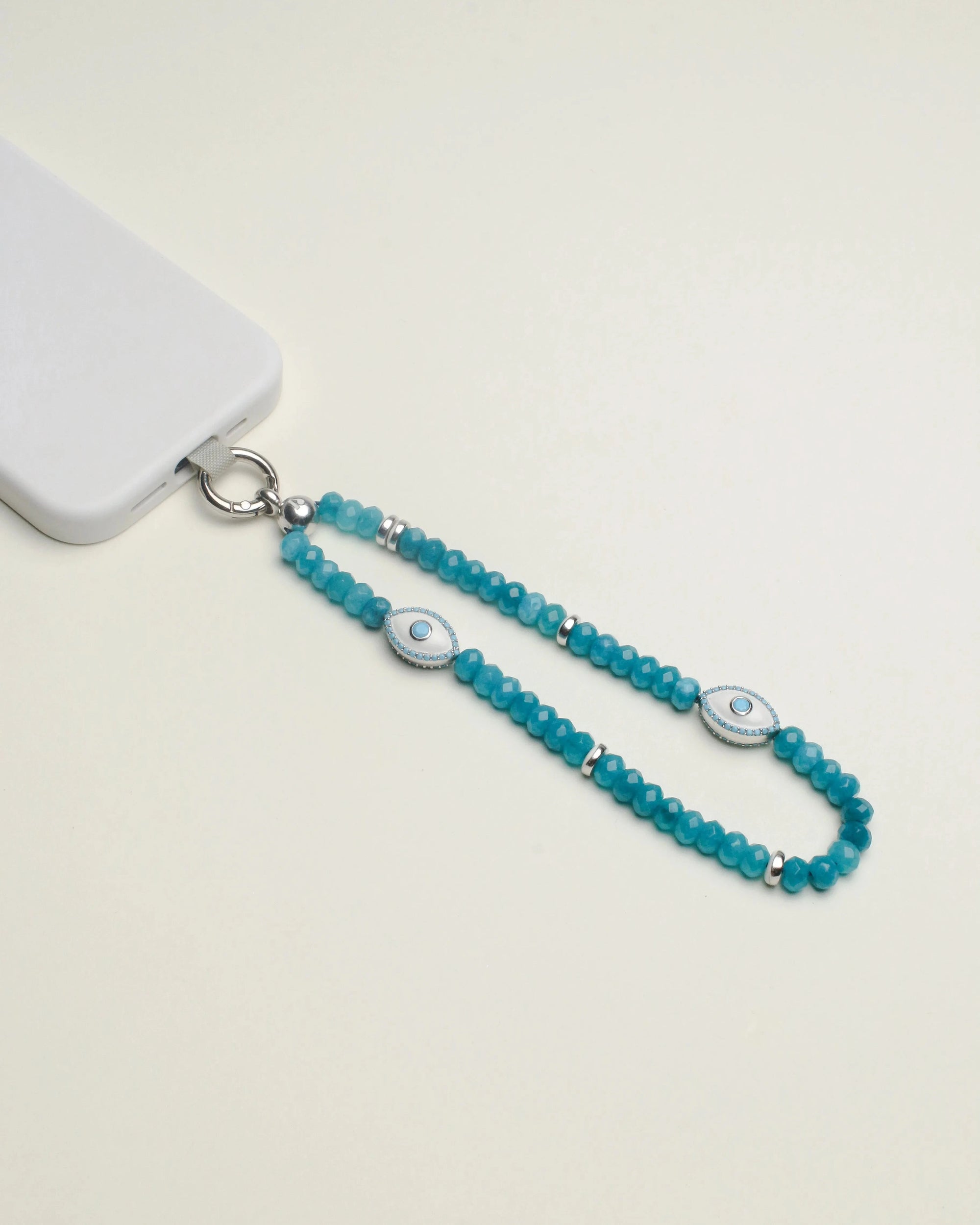 Stella phone wristlet crafted with turquoise beads and adorned with an elegant evil eye charm, attached to a white phone for a stylish touch.