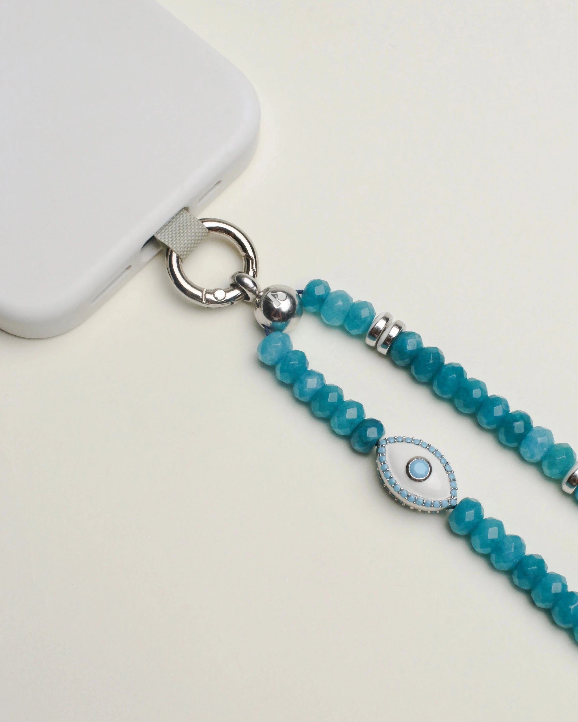 Detailed view of the Stella wristlet in turquoise quartz, featuring the evil eye charm for protective energy, shown connected to a white phone.