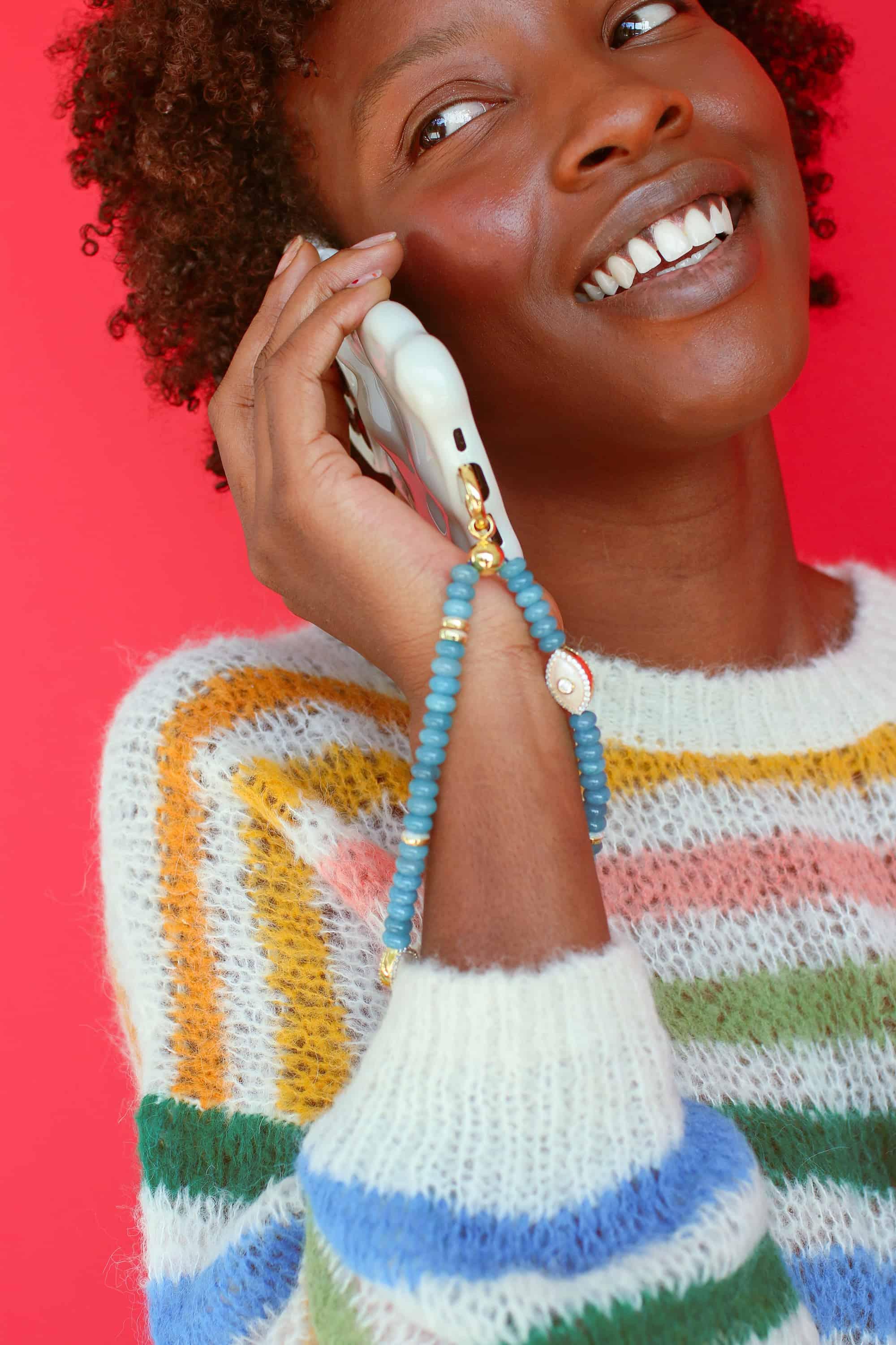 a woman holding a white mobile phone with a turquoise quartz wristlet phone strap