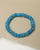 Single Zoe bracelet in azure blue laid flat, featuring smooth beads and gold accents for an elegant look.