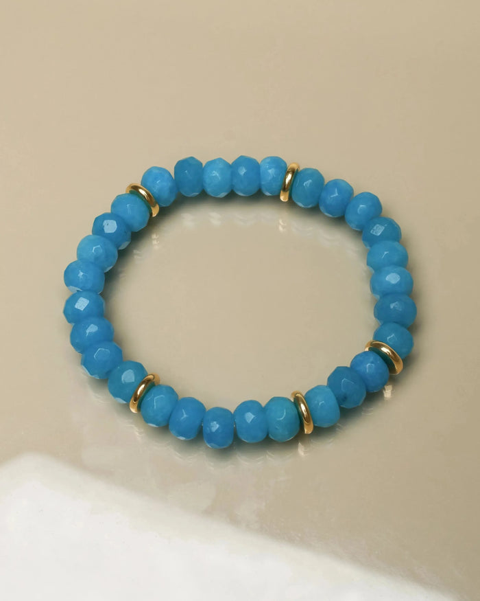 Single Zoe bracelet in azure blue laid flat, featuring smooth beads and gold accents for an elegant look.