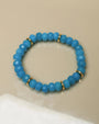 Single Zoe bracelet in azure blue laid flat, featuring smooth beads and gold accents for an elegant look.