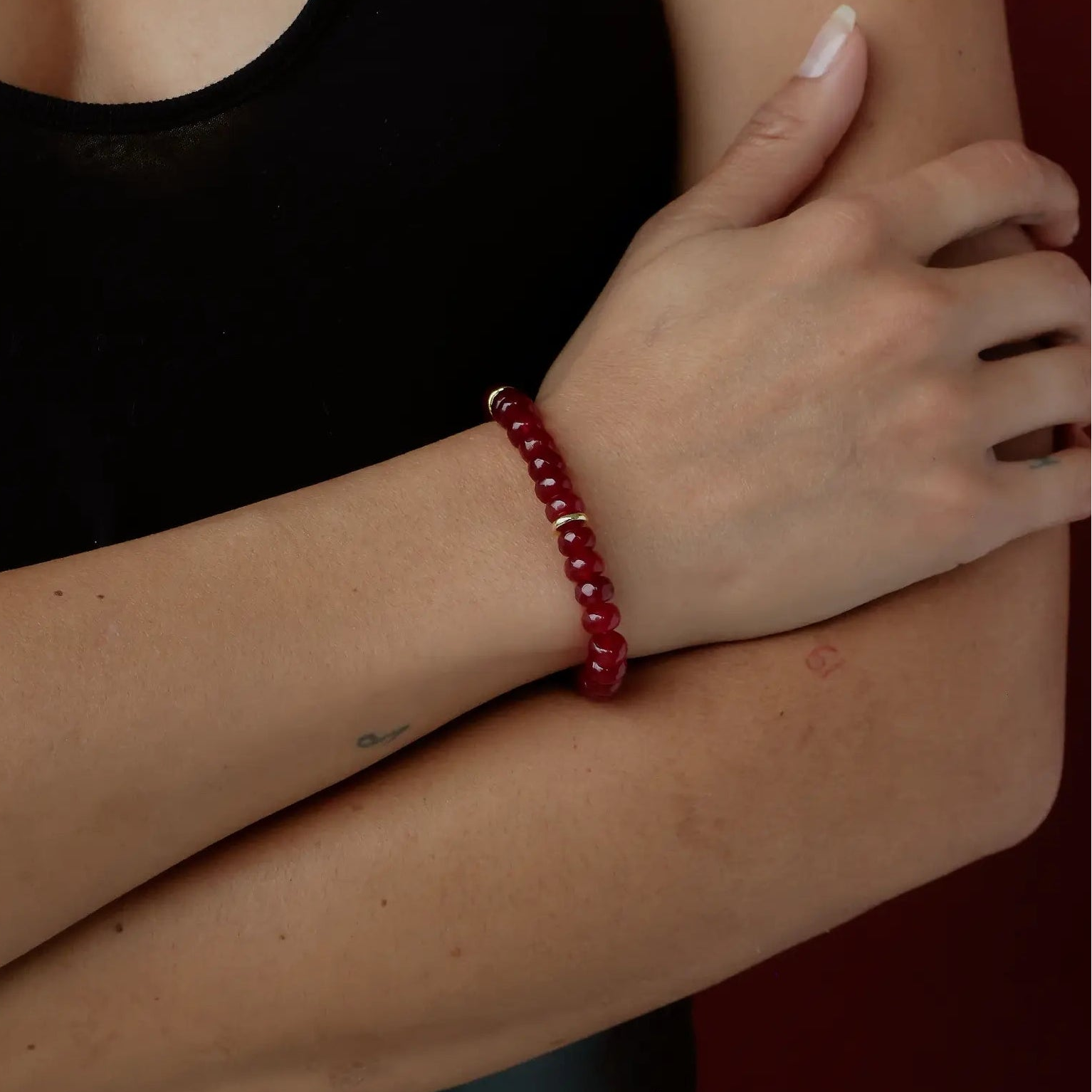 Woman wearing a black tank top and red beaded jewelry against a dark background
