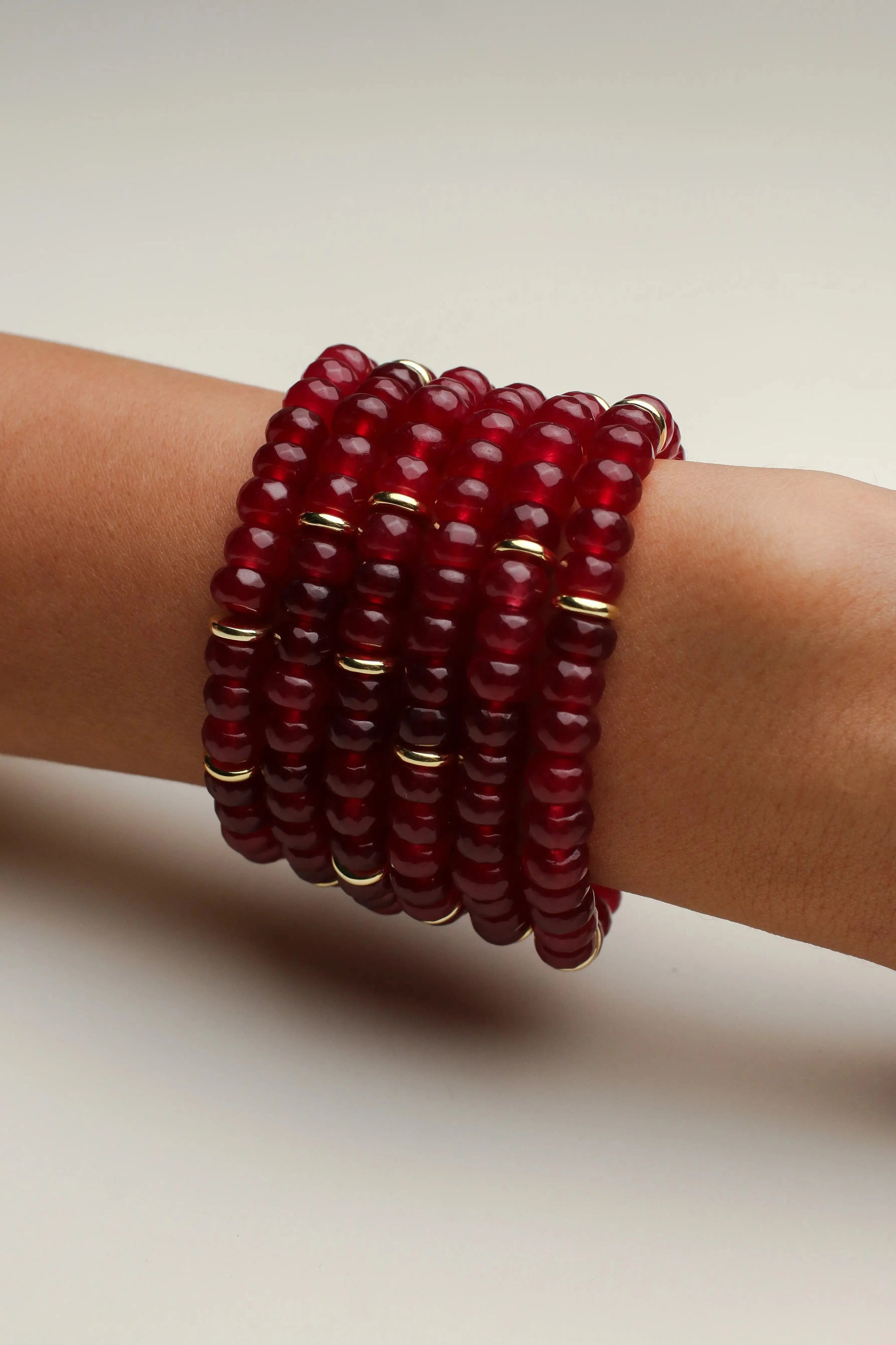 Six Zoe cherry quartz bracelets displayed wrapped around a cylindrical stand, emphasizing their rich red color and gold accents.