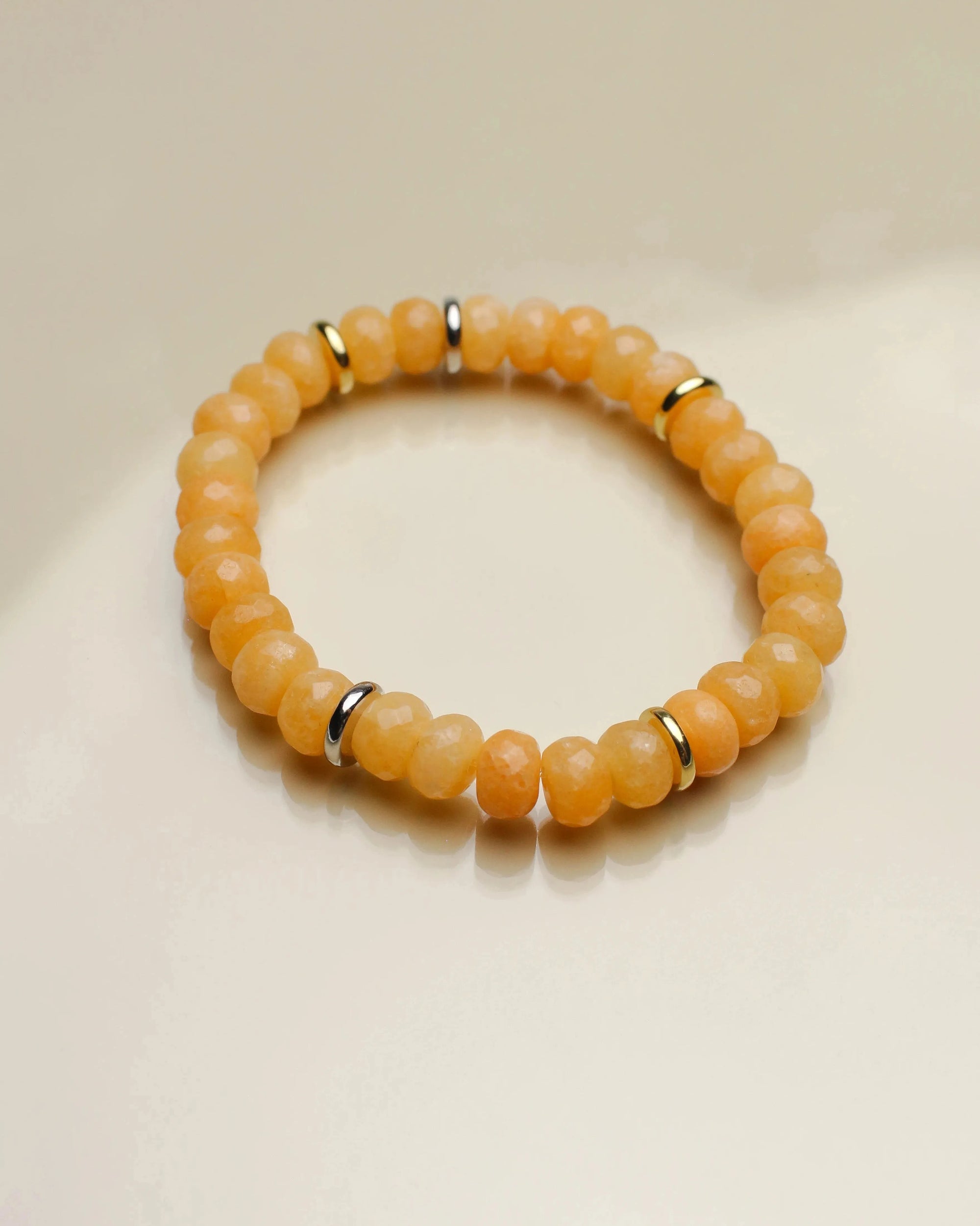 Single Zoe bracelet in tangerine quartz with gold accents, arranged in a circular shape on a flat surface.