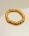 Single Zoe bracelet in tangerine quartz with gold accents, arranged in a circular shape on a flat surface.