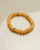 Single Zoe bracelet in tangerine quartz with gold accents, arranged in a circular shape on a flat surface.