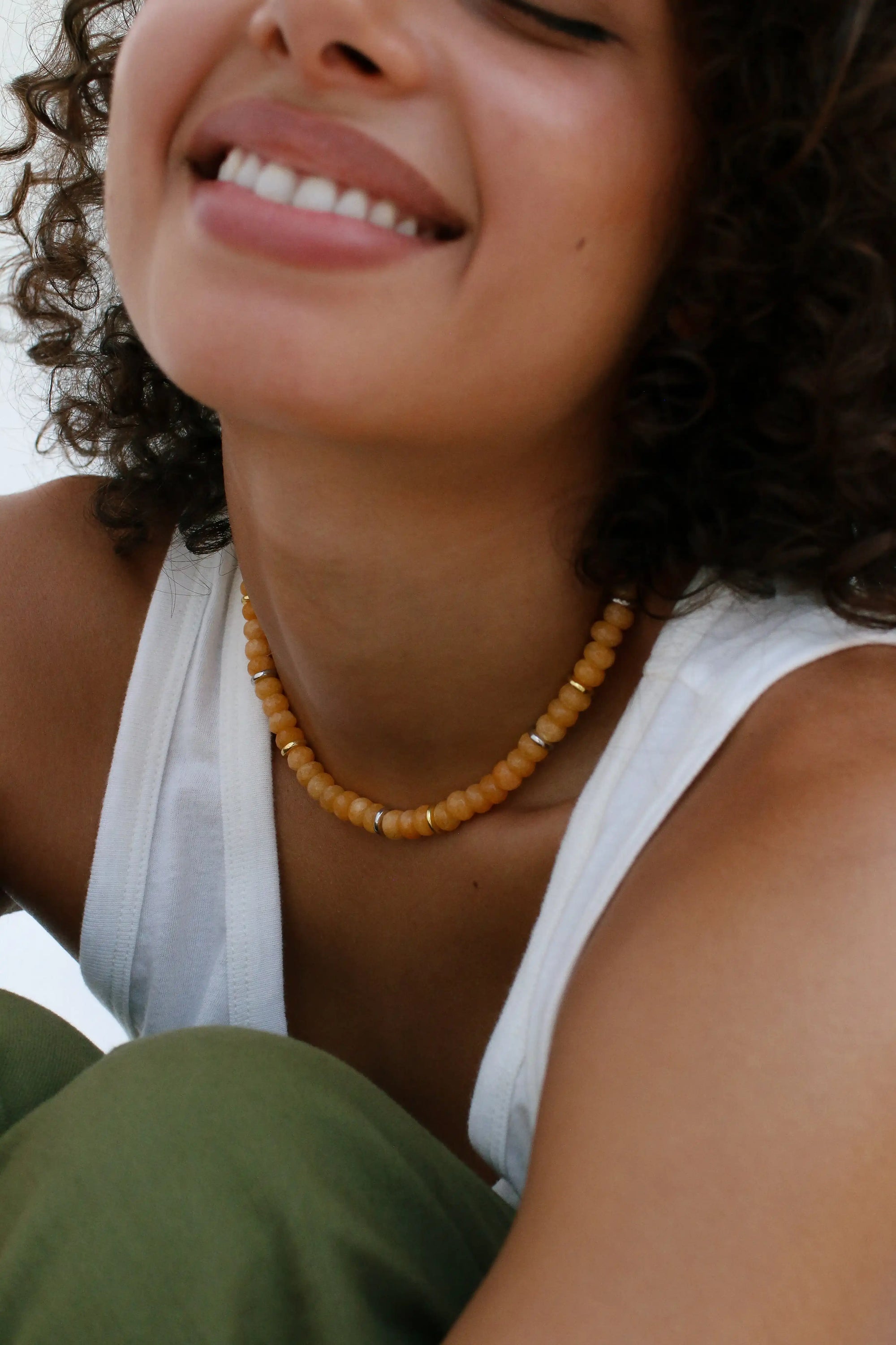 A smiling model wearing the Zoe necklace in tangerine quartz, adding a bright, sunny pop of color to her outfit.